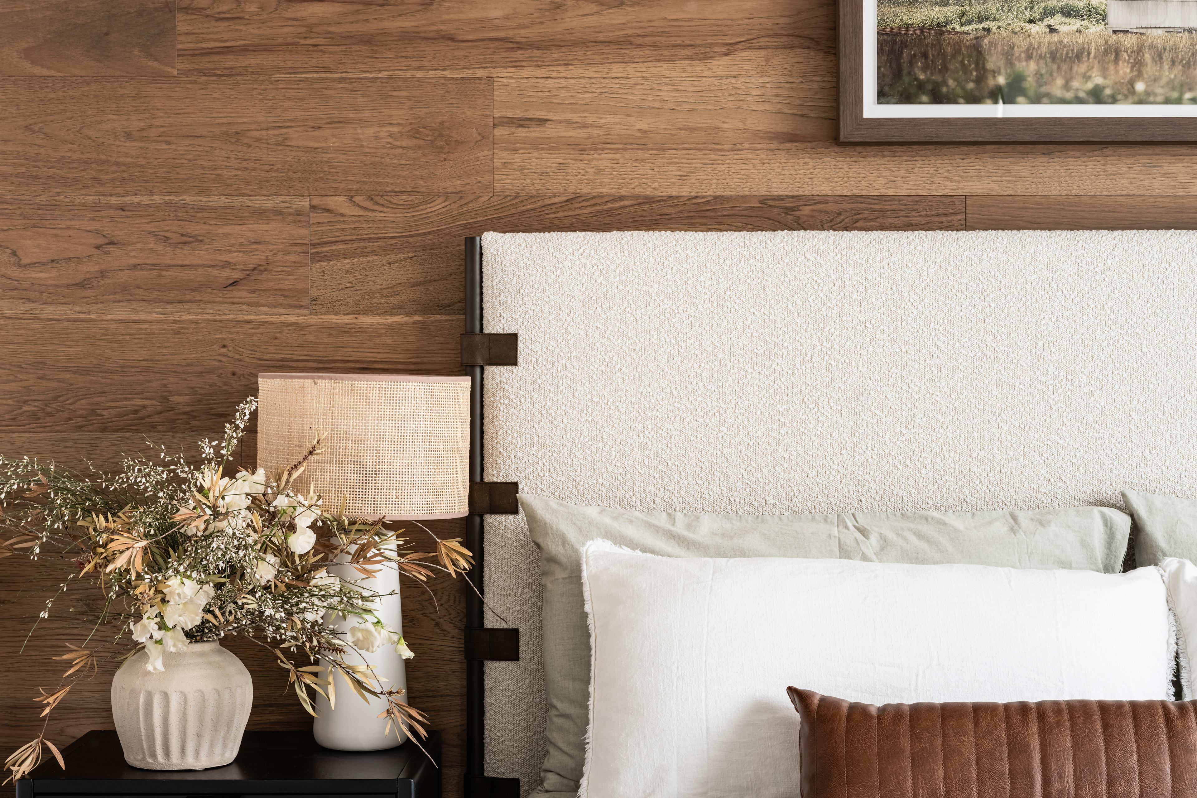 A cozy and inviting bedroom with a wooden accent wall, a white bed with plush bedding, and a framed artwork on the wall, complemented by decorative elements on the nightstand.