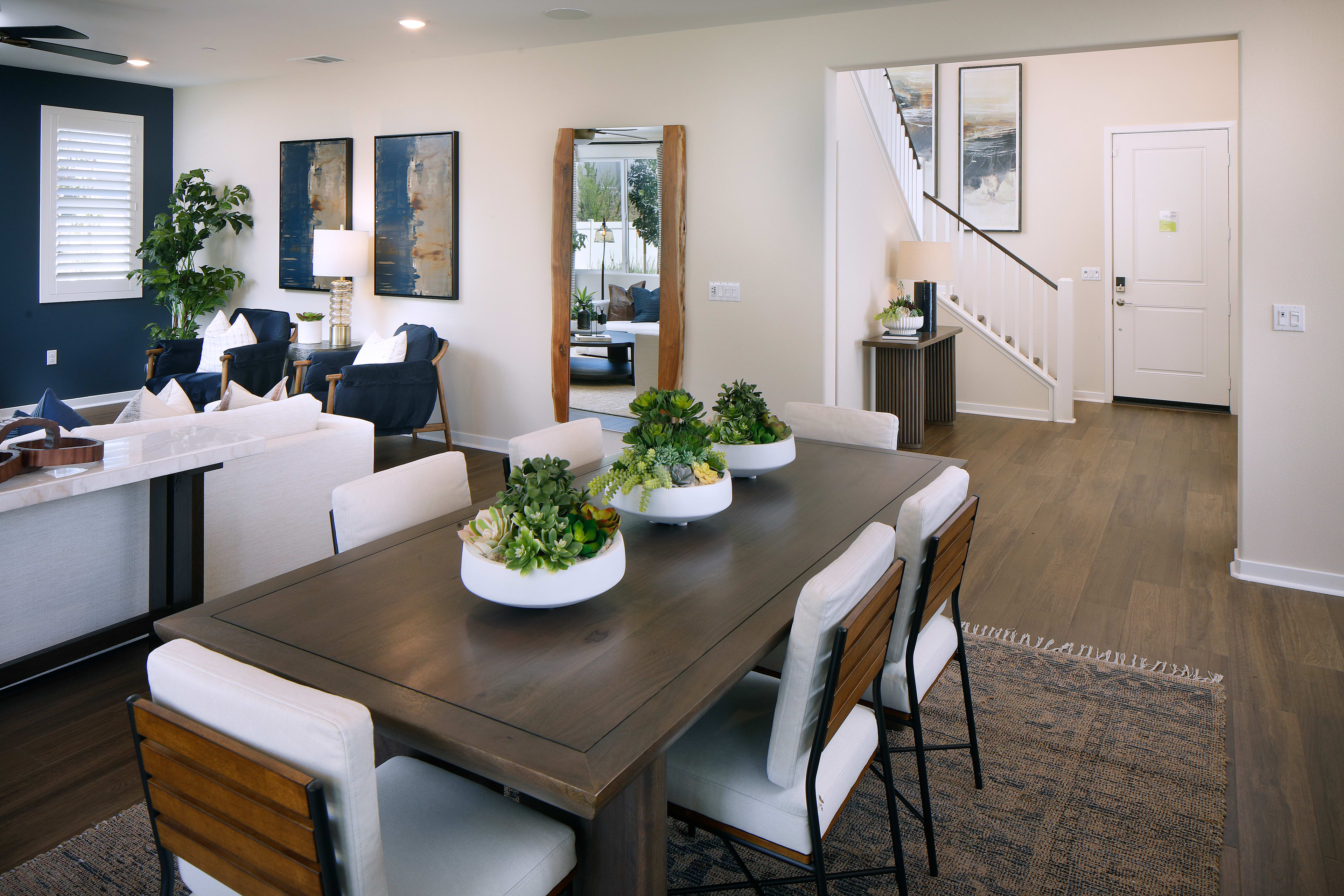 A modern and stylish dining room with a wooden table, white chairs, and various decorative elements such as plants and mirrors adorning the walls.