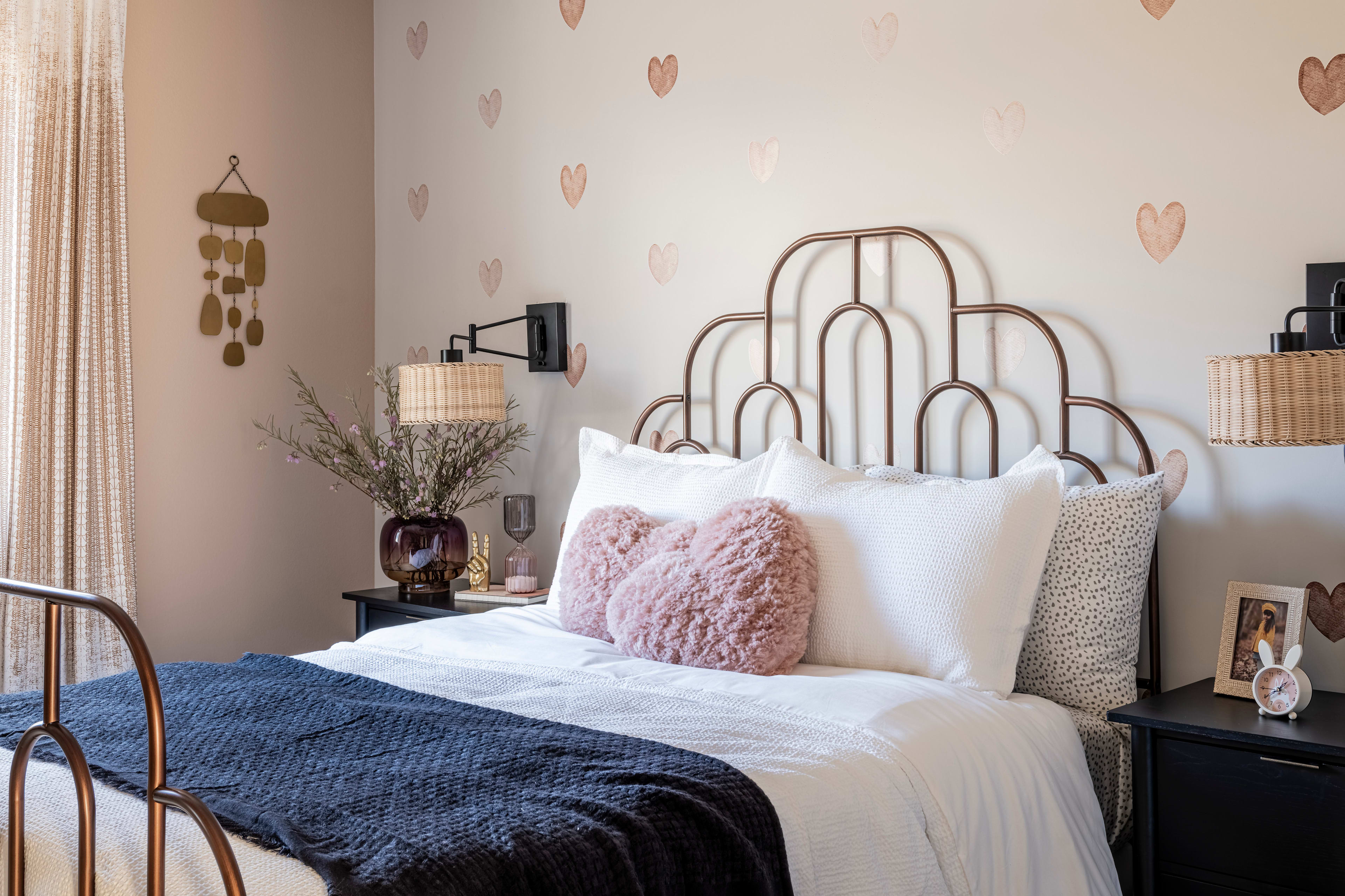 A cozy and inviting bedroom with a white metal bed frame, plush bedding, and decorative heart-shaped wall decals creating a warm and romantic atmosphere.