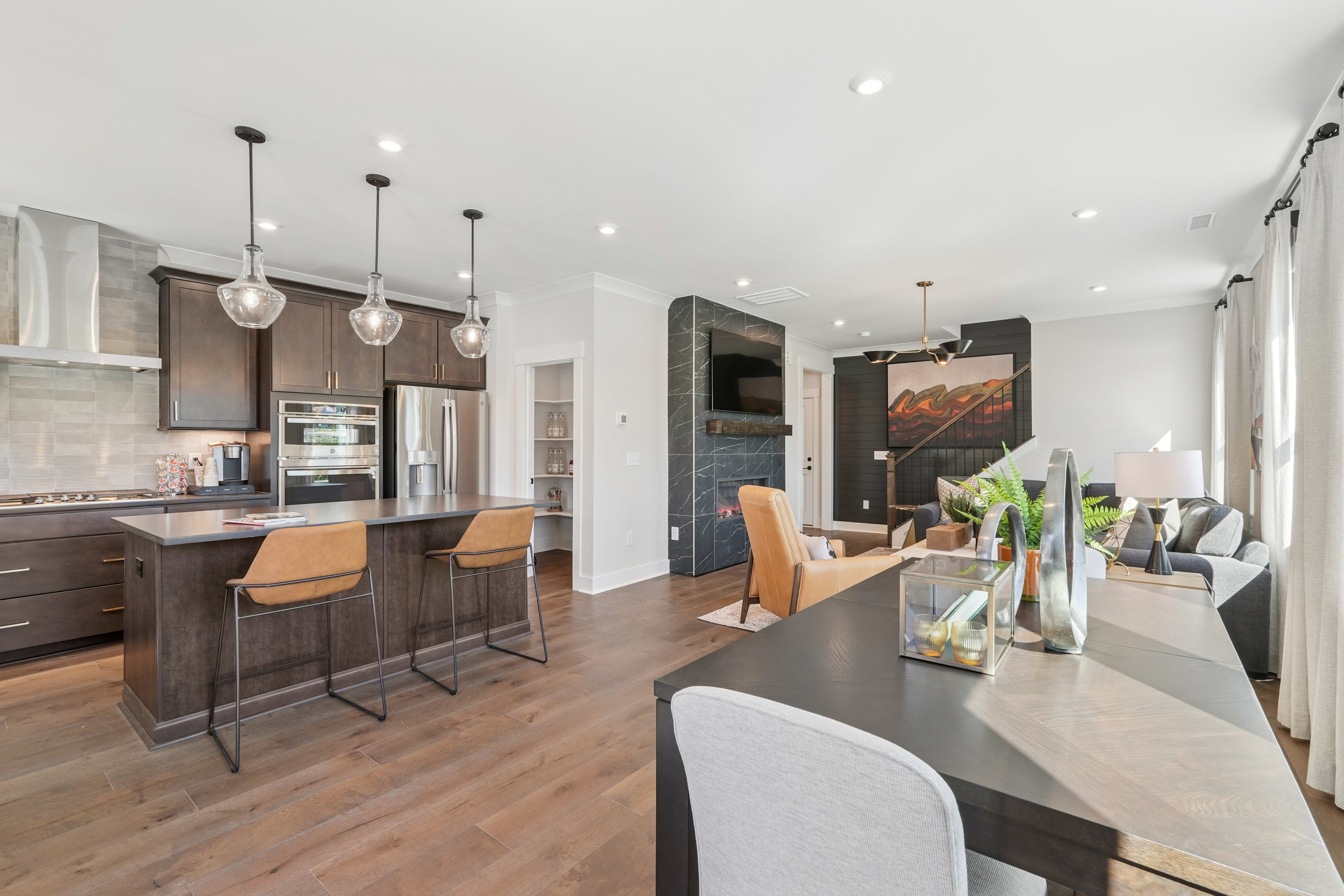 A modern and spacious kitchen with a dining area, featuring dark wood cabinets, pendant lighting, and a large window providing natural light.