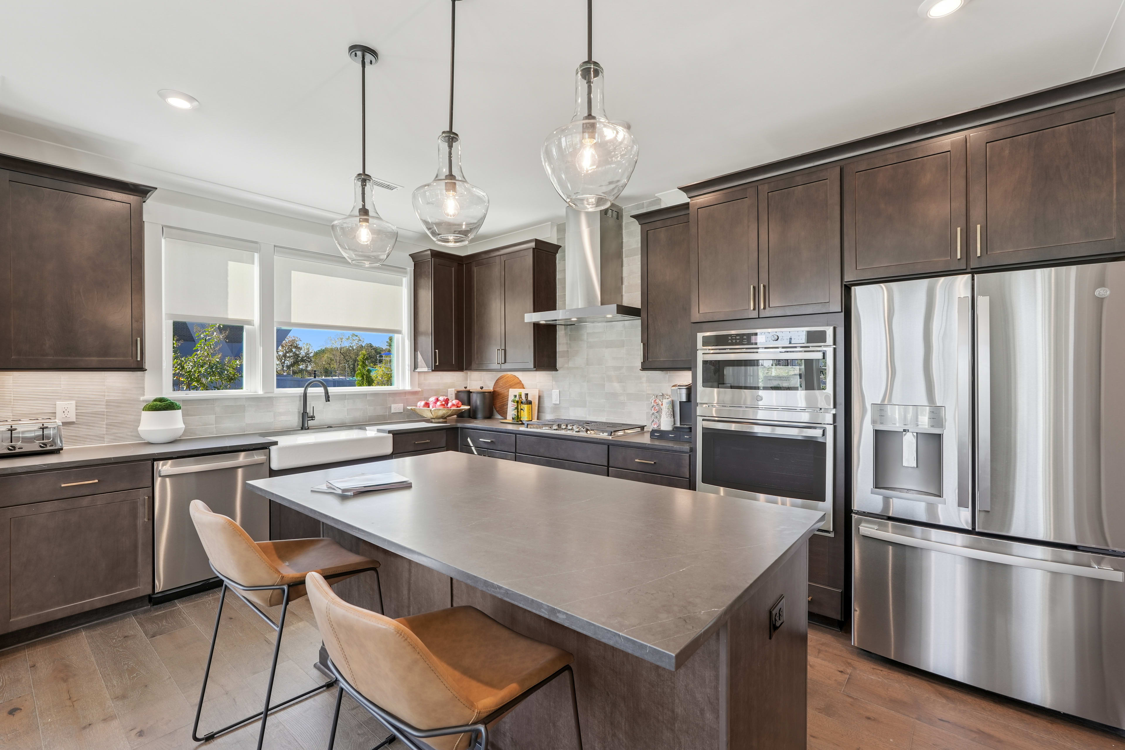 A modern, well-equipped kitchen with dark wood cabinets, stainless steel appliances, and pendant lighting over a central island with bar stools.