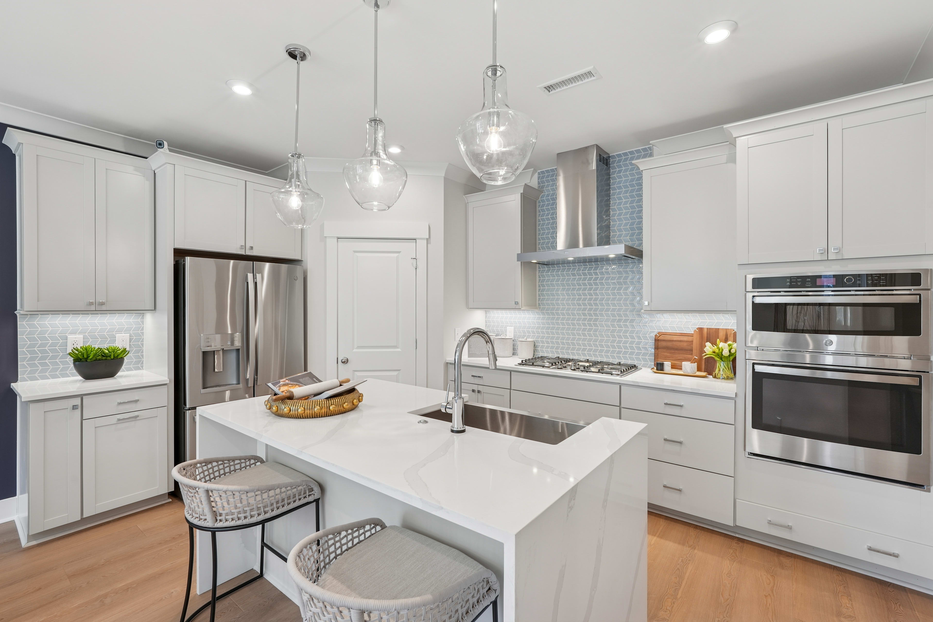 A modern, bright, and spacious kitchen with white cabinets, stainless steel appliances, a large island with stools, and pendant lighting fixtures.