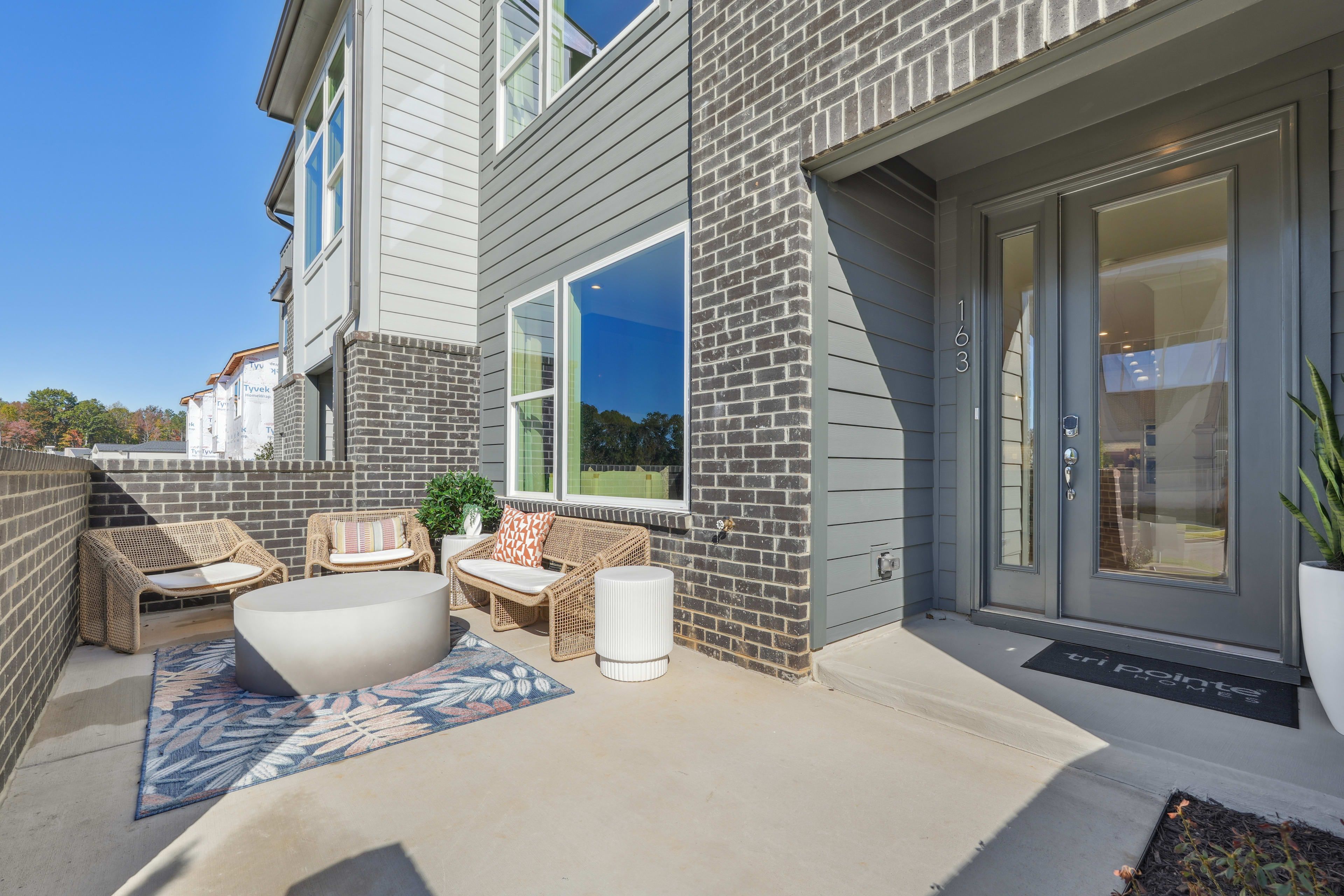 A cozy outdoor seating area with wicker furniture and decorative elements, set against a backdrop of a modern, brick-accented residential building.