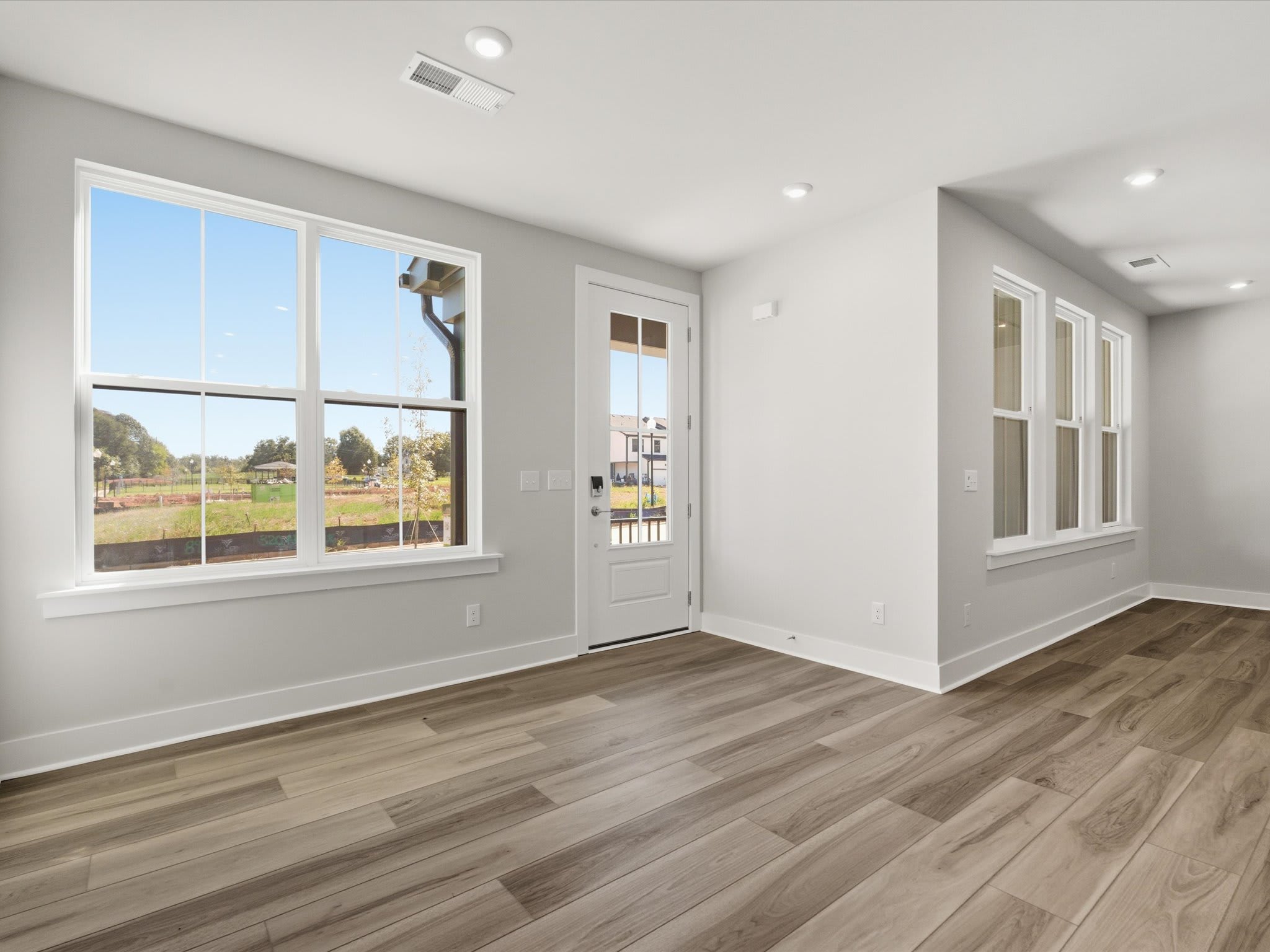 A spacious, well-lit room with large windows overlooking a scenic outdoor landscape, featuring hardwood flooring and a white interior design.