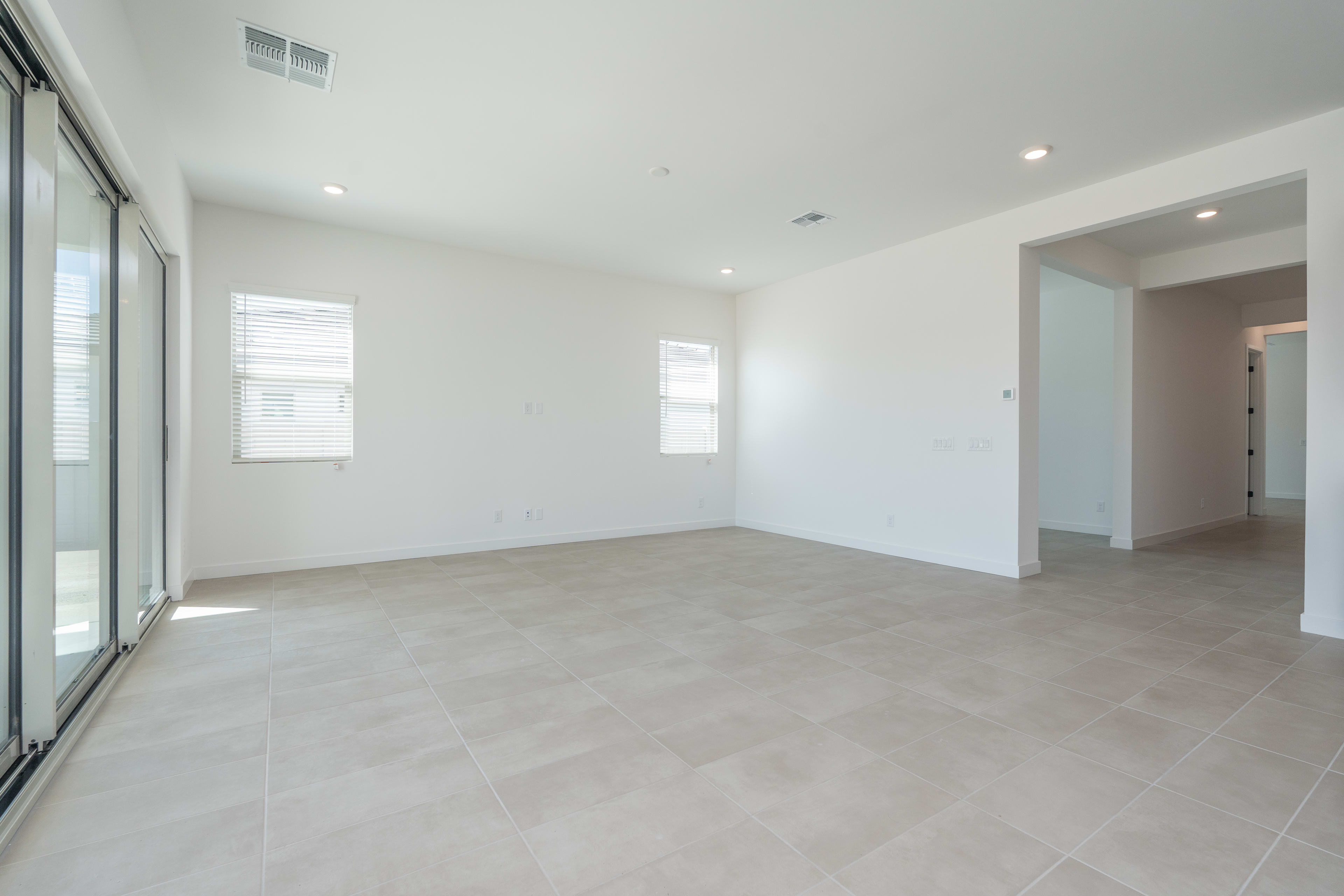 A spacious, minimalist room with large windows, light-colored tile flooring, and recessed lighting in the ceiling.
