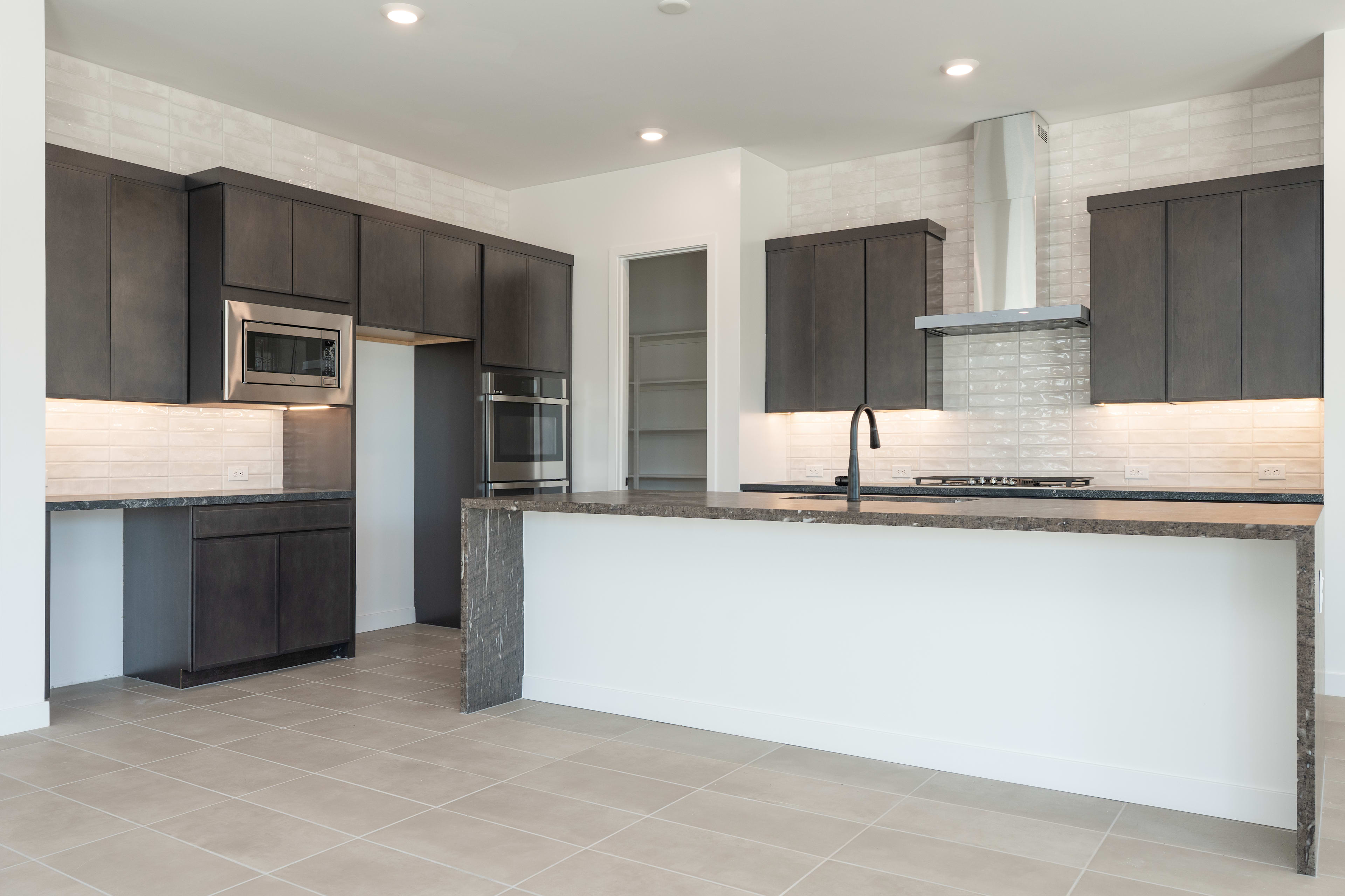 A modern, open-concept kitchen with dark cabinets, a white countertop, and a tiled floor.