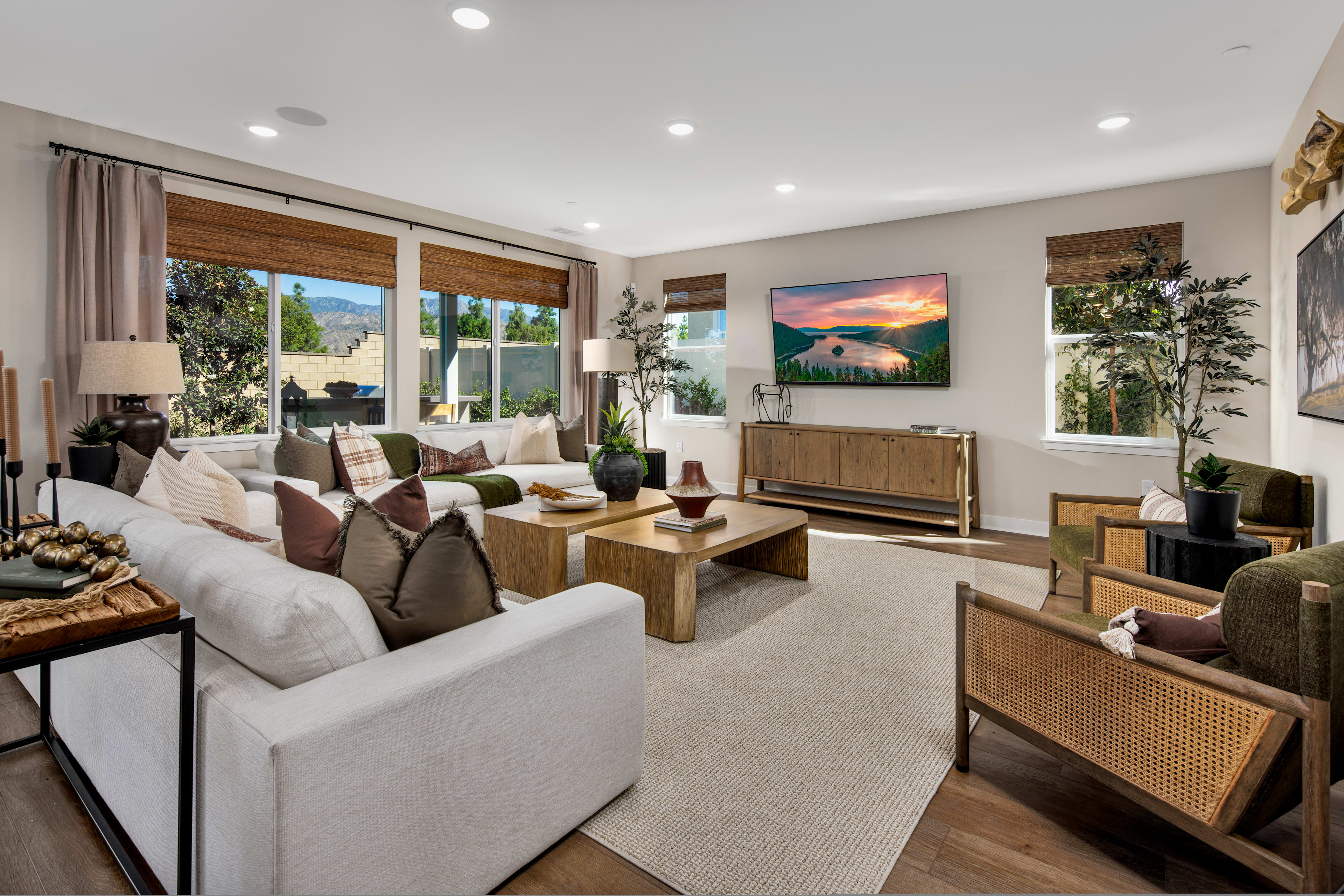 A cozy and inviting living room with plush white sofas, wooden furniture, and a large landscape painting on the wall, overlooking a scenic outdoor view through the large windows.