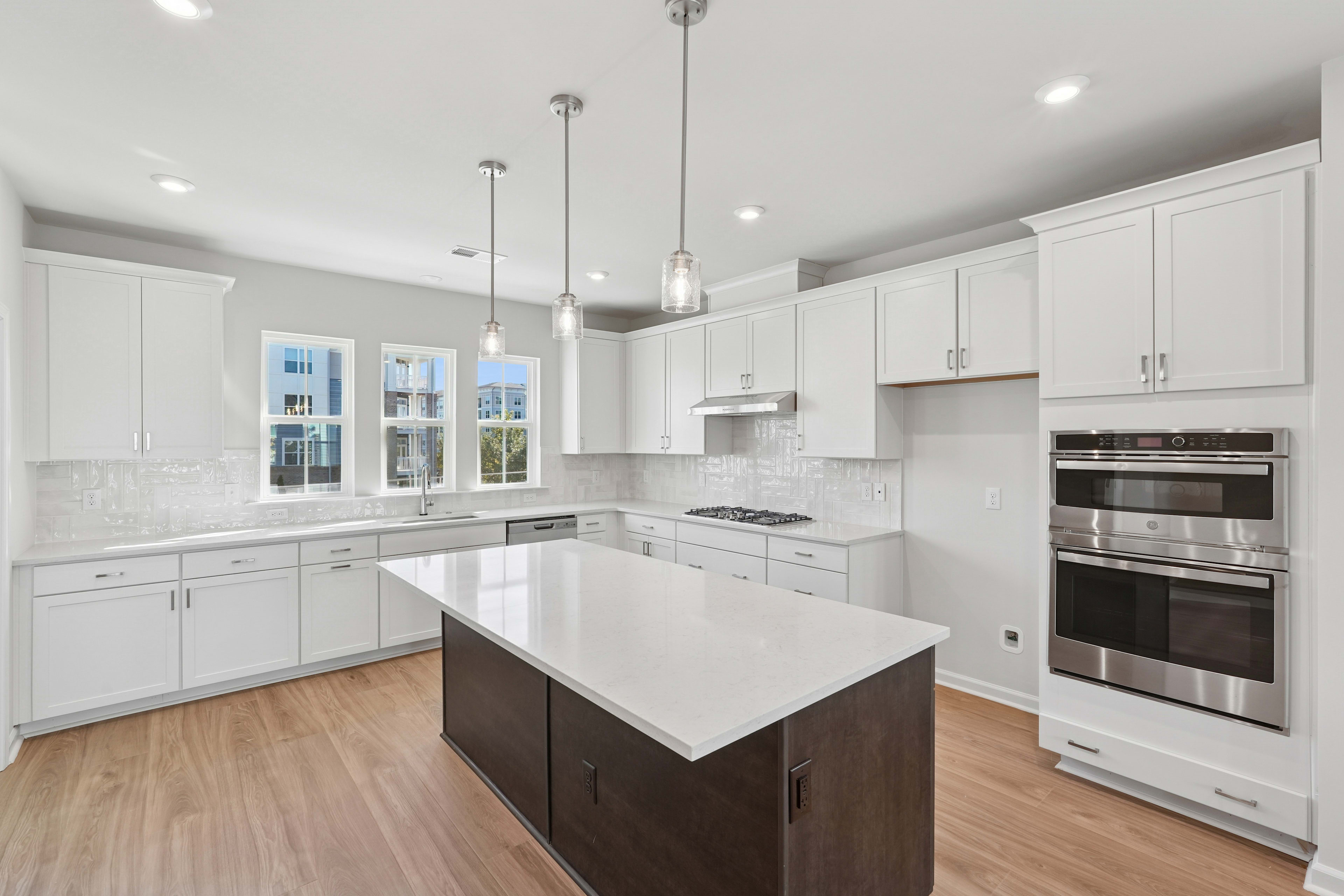 A modern, well-lit kitchen with white cabinets, stainless steel appliances, and a dark-colored kitchen island in the foreground.