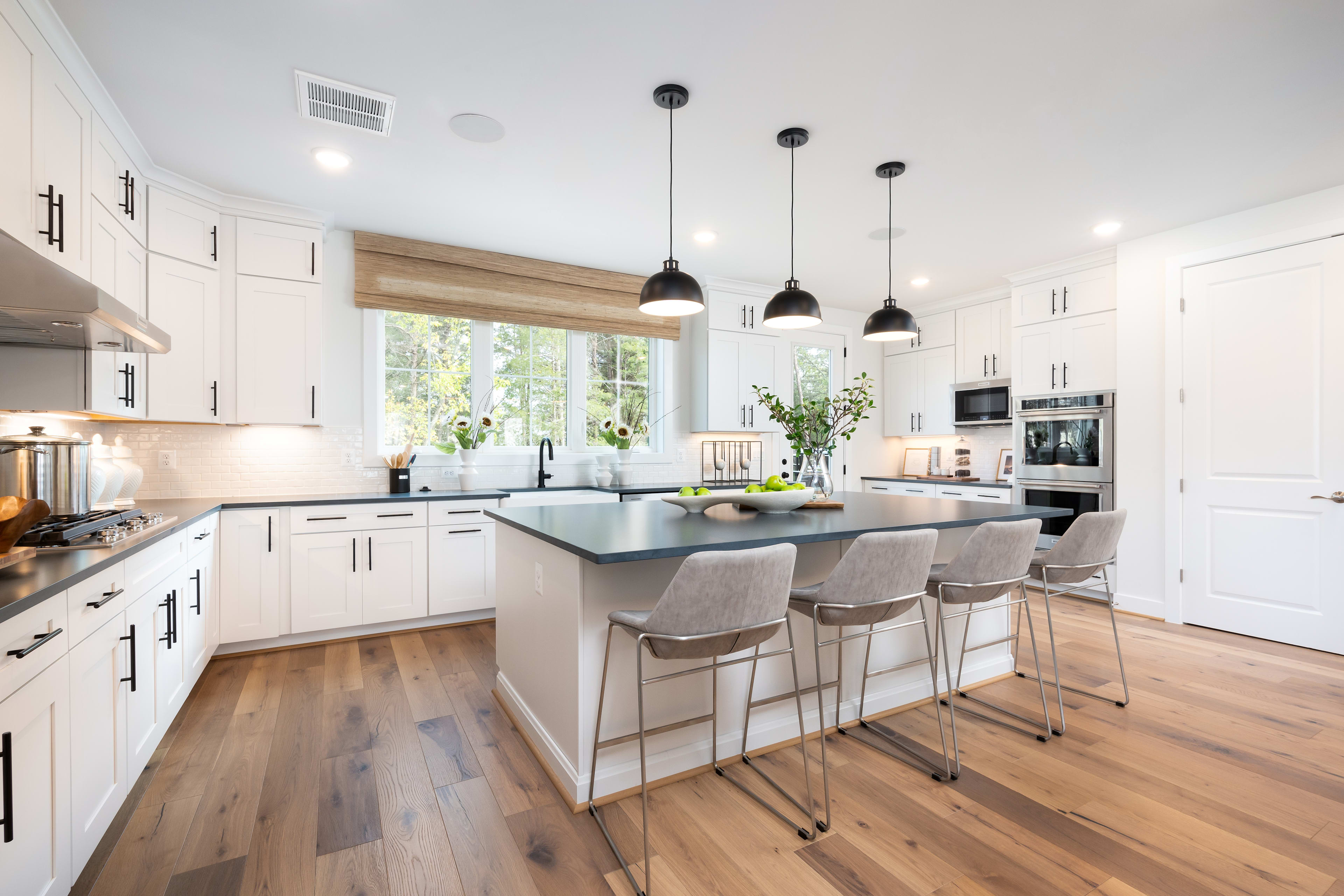 A modern, bright, and spacious kitchen with white cabinets, a large island with bar stools, and pendant lights hanging above.