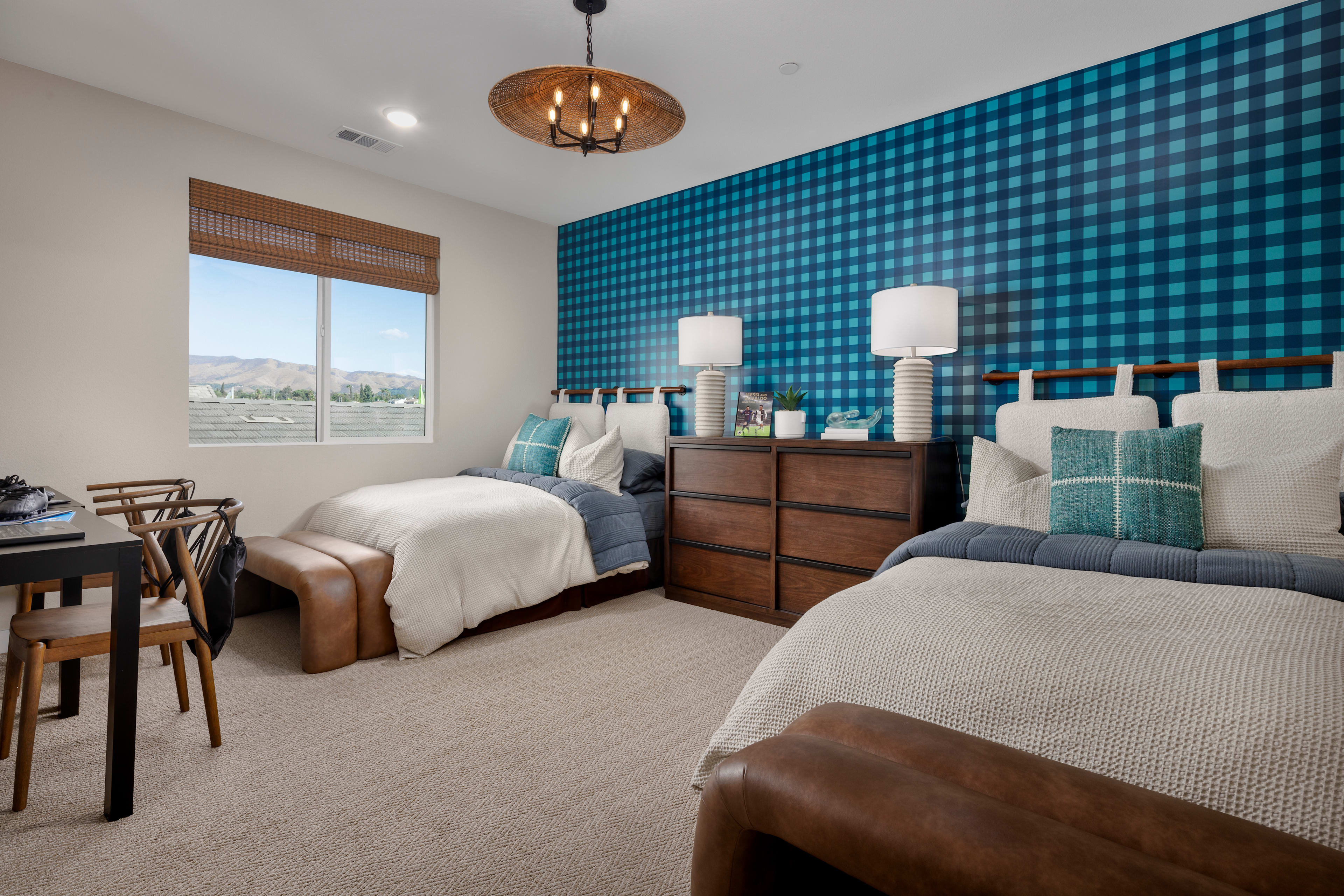 A cozy bedroom with a blue and white checkered accent wall, a wooden dresser, and two twin beds with neutral bedding.