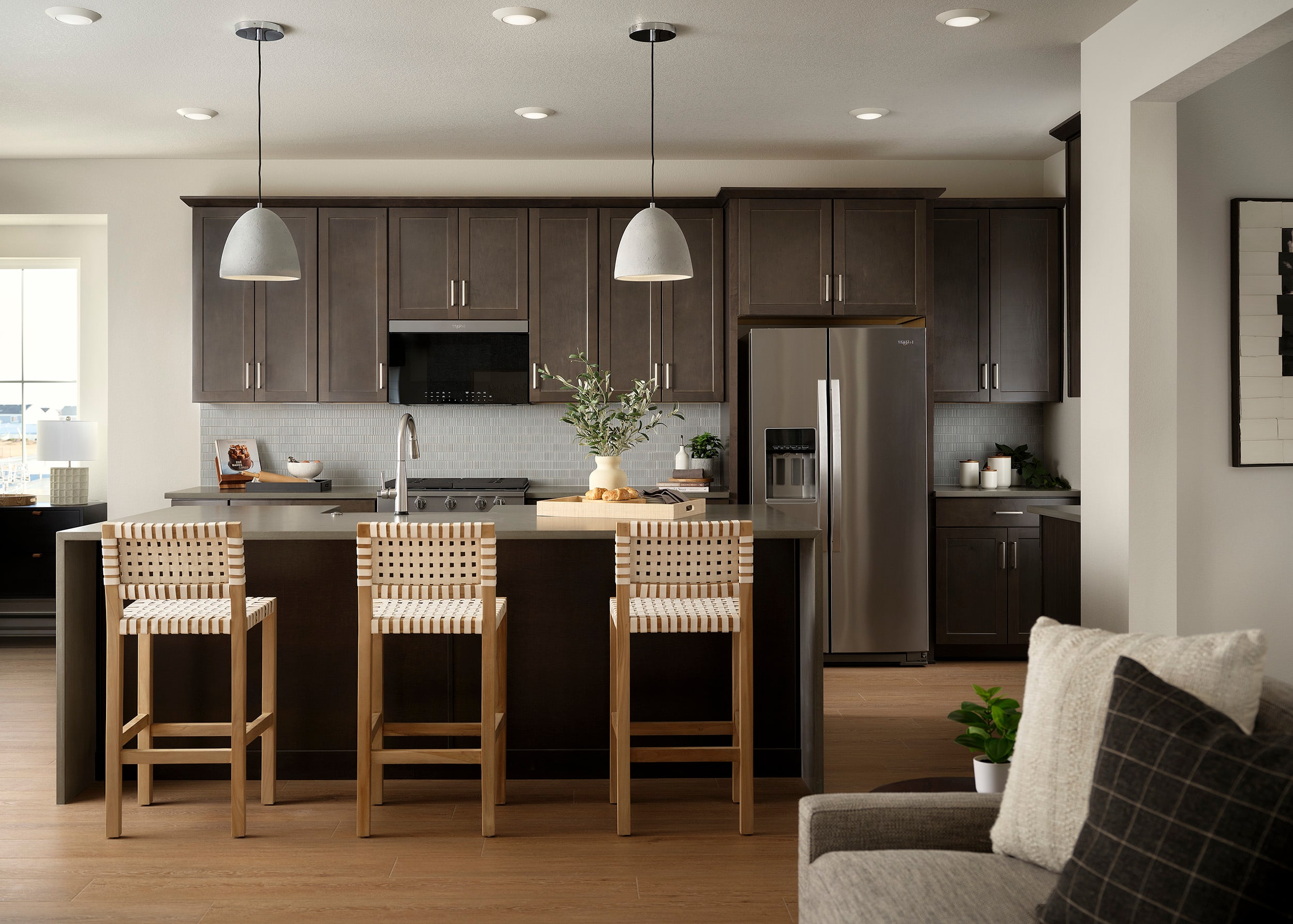A modern and well-appointed kitchen with dark wood cabinets, stainless steel appliances, and a central island with bar stools, complemented by a cozy living area in the background.