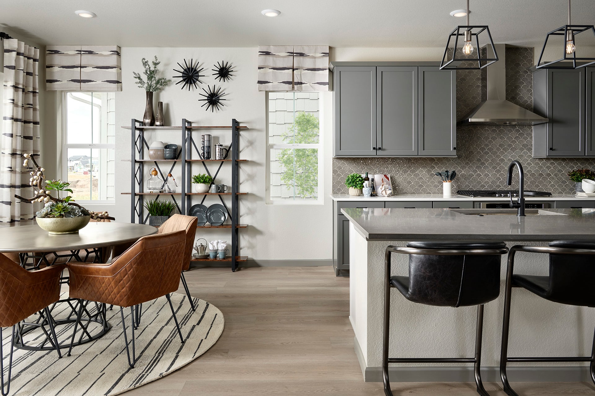 A modern and stylish kitchen with a dining area, featuring gray cabinets, a patterned backsplash, and various decorative elements such as wall art and potted plants.