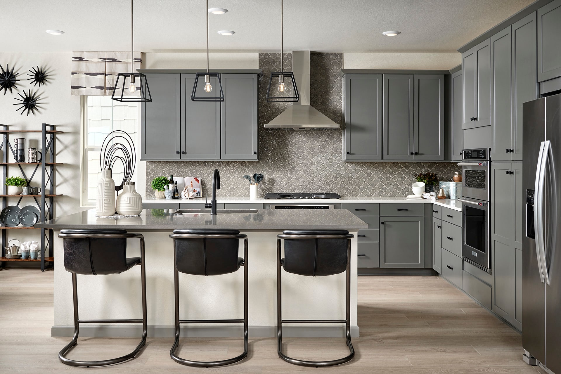 A modern and stylish kitchen with gray cabinets, a kitchen island with three bar stools, and various lighting fixtures and decor elements.