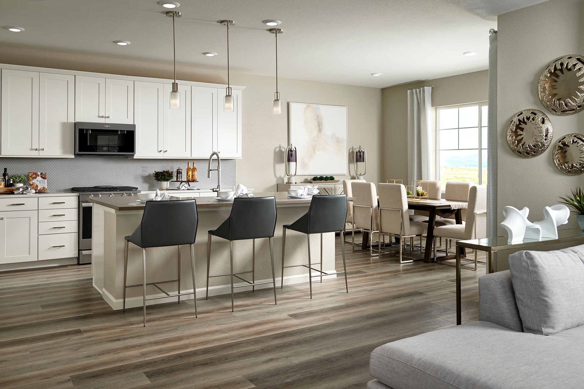 A modern and spacious kitchen with white cabinets, a large island with bar stools, and a dining area with a wooden table and chairs, all set against a neutral color scheme and accented with decorative wall pieces.