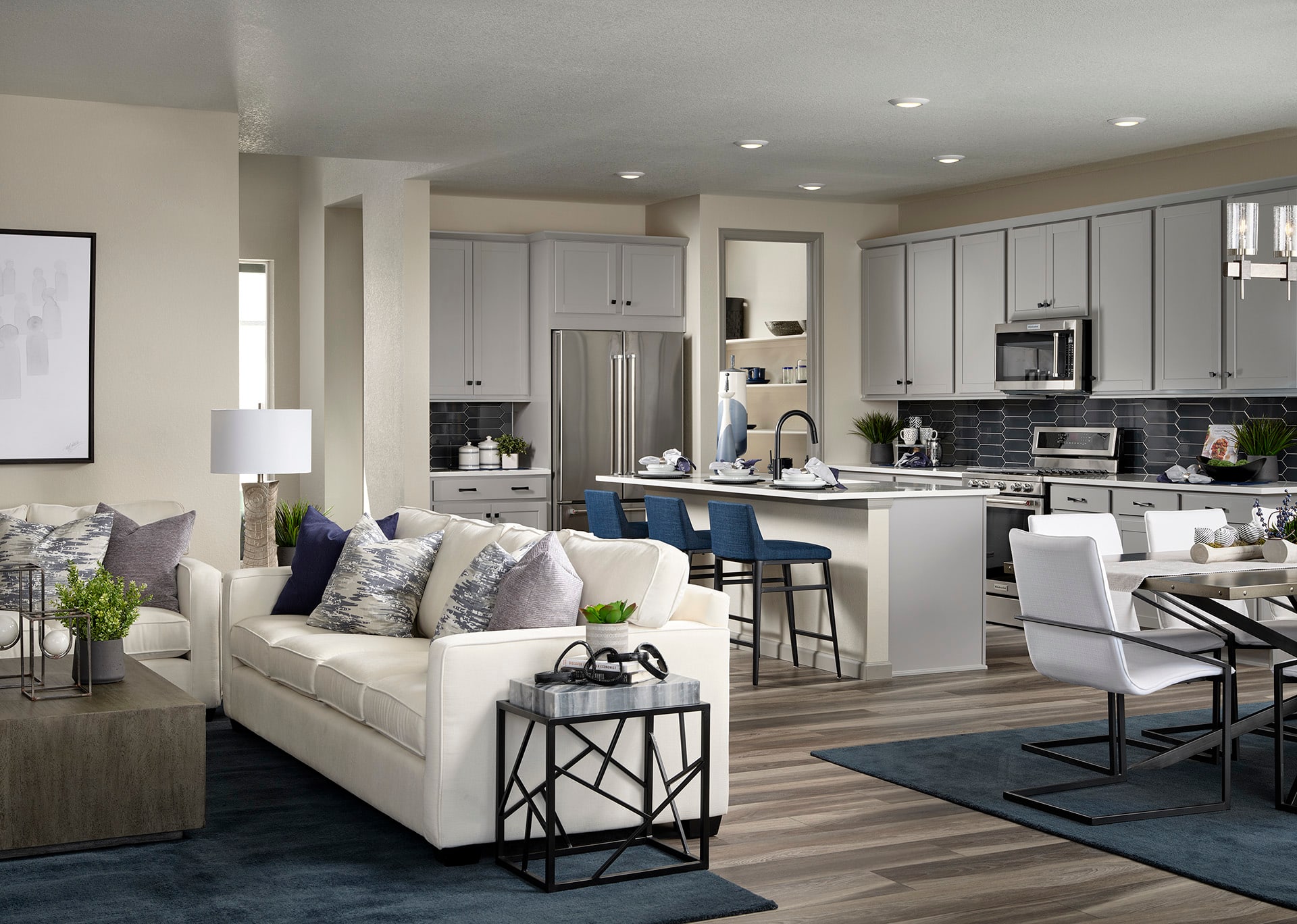 A modern and spacious open-concept kitchen and living room with white cabinets, stainless steel appliances, and a comfortable white sofa in the foreground.
