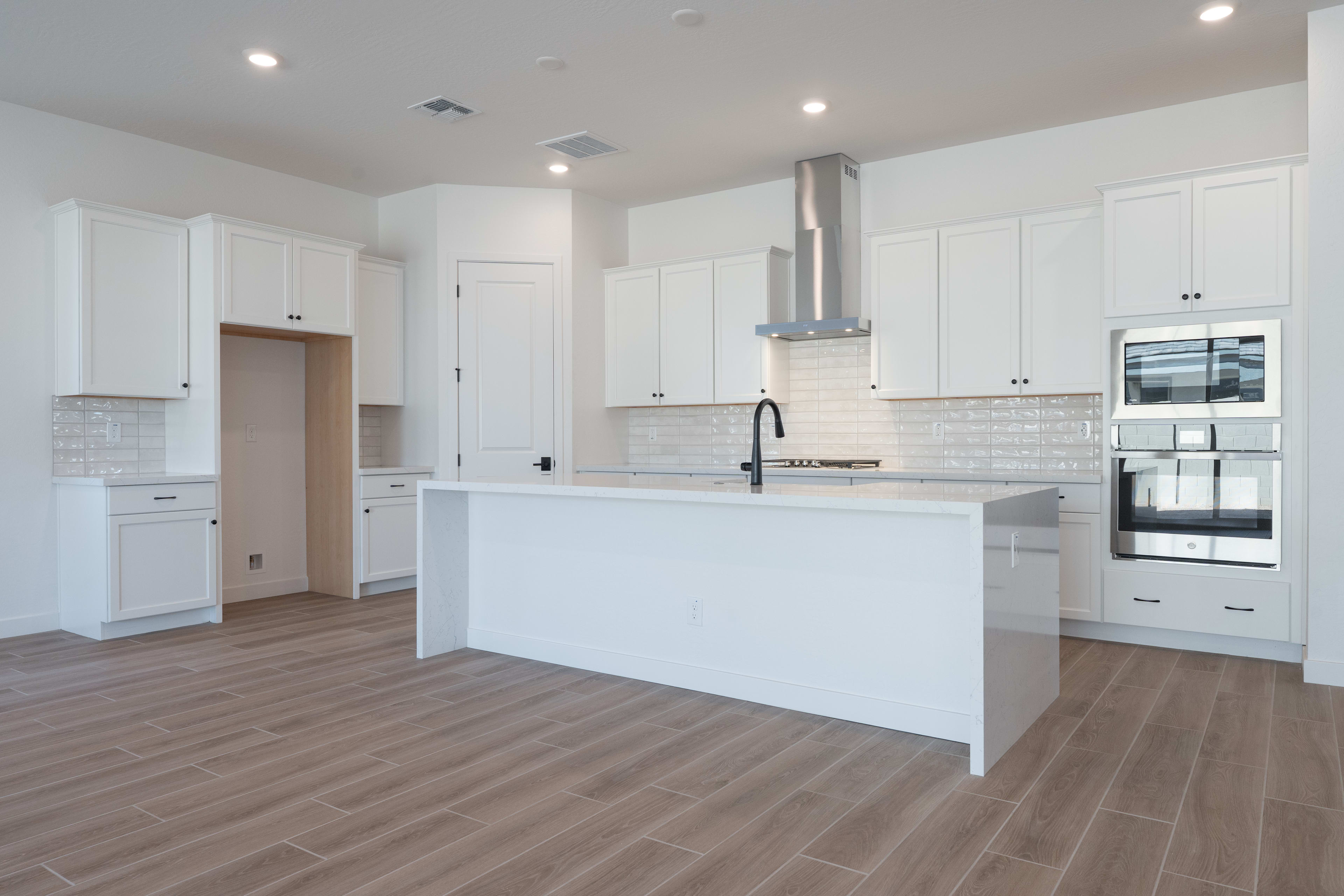 A modern, open-concept kitchen with white cabinets, a central island, and hardwood-style flooring.