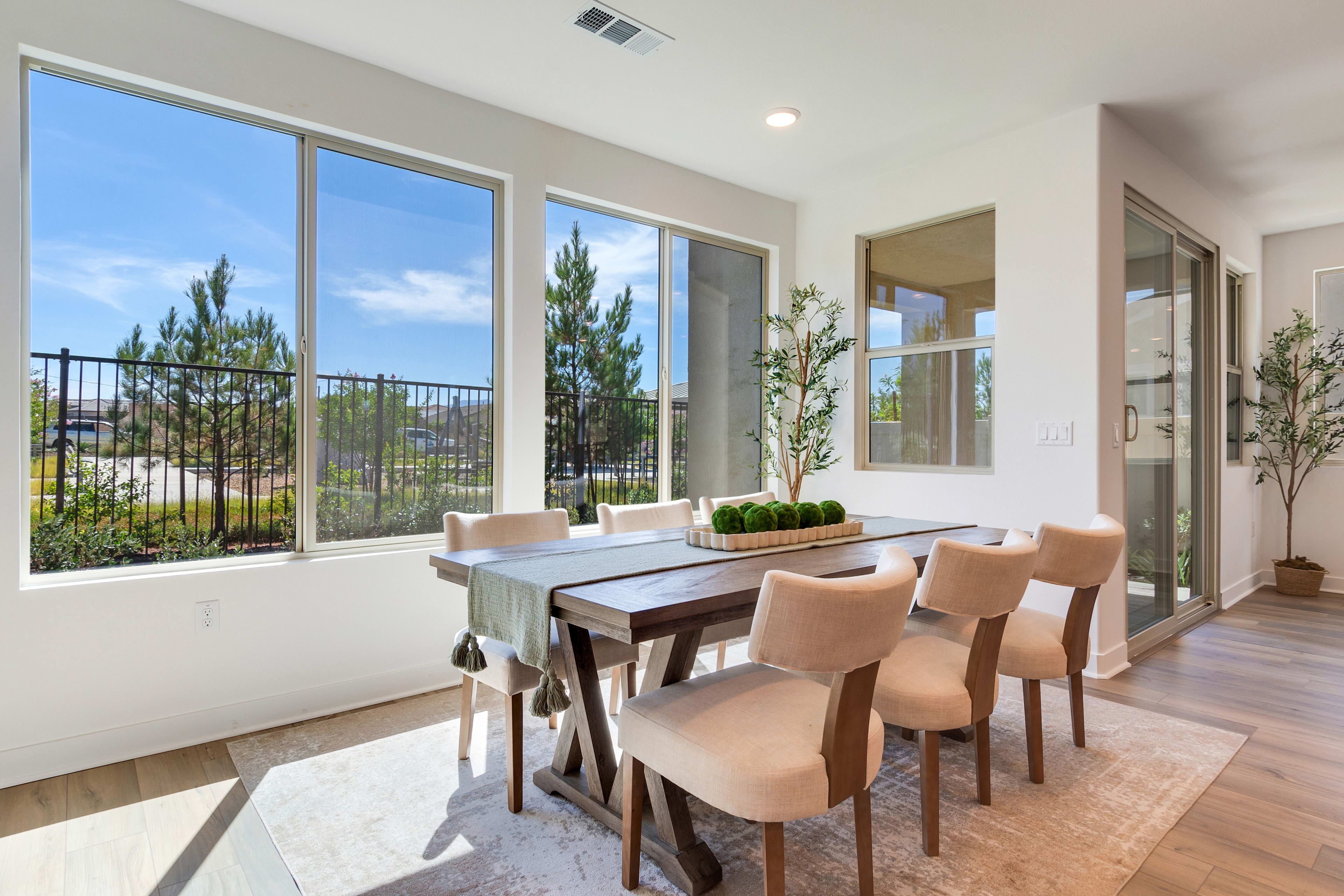 A modern and spacious dining room with large windows overlooking a scenic outdoor landscape featuring pine trees and a clear sky.