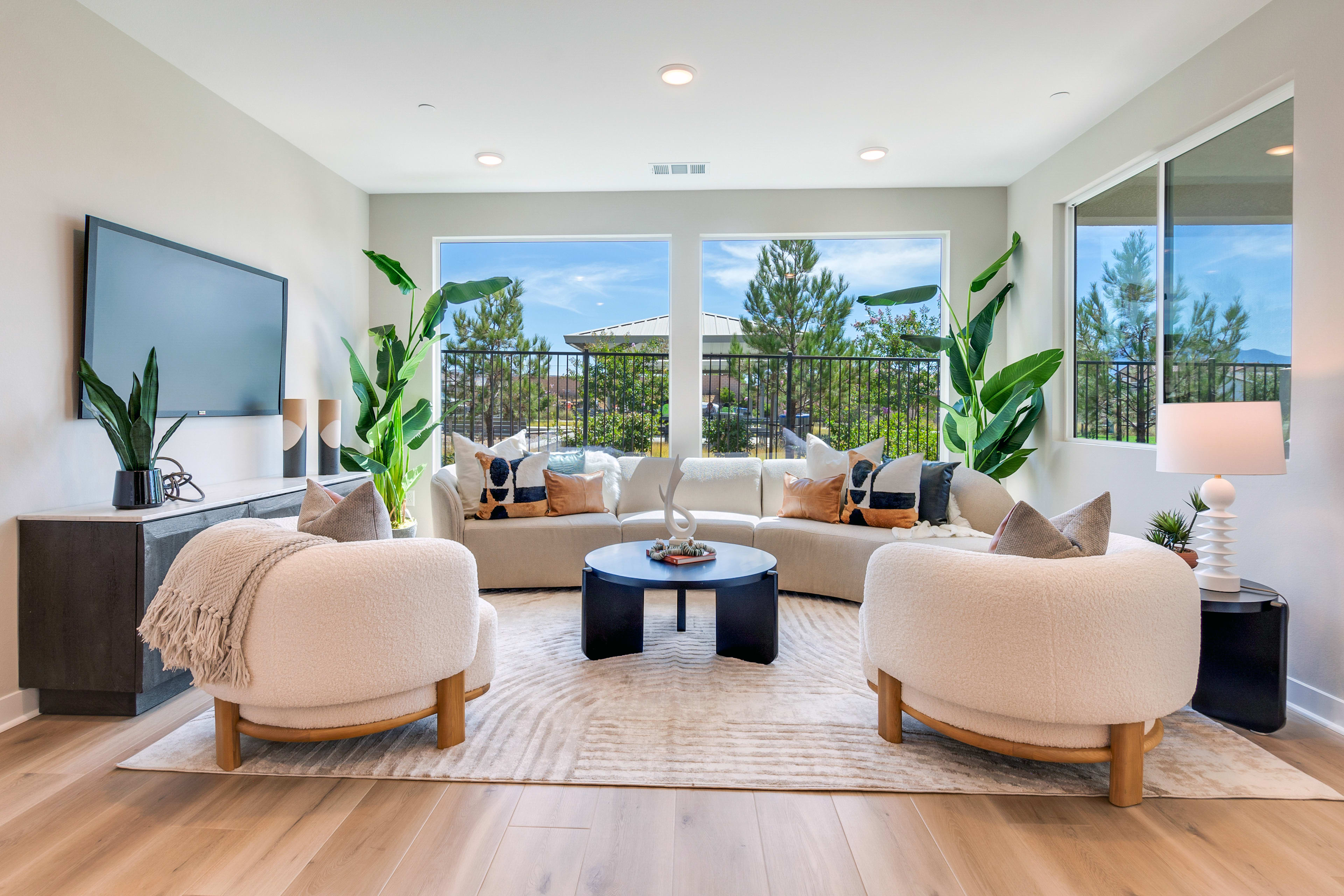 A spacious and modern living room with large windows overlooking a scenic outdoor landscape, featuring comfortable seating arrangements, a television, and various decorative elements.