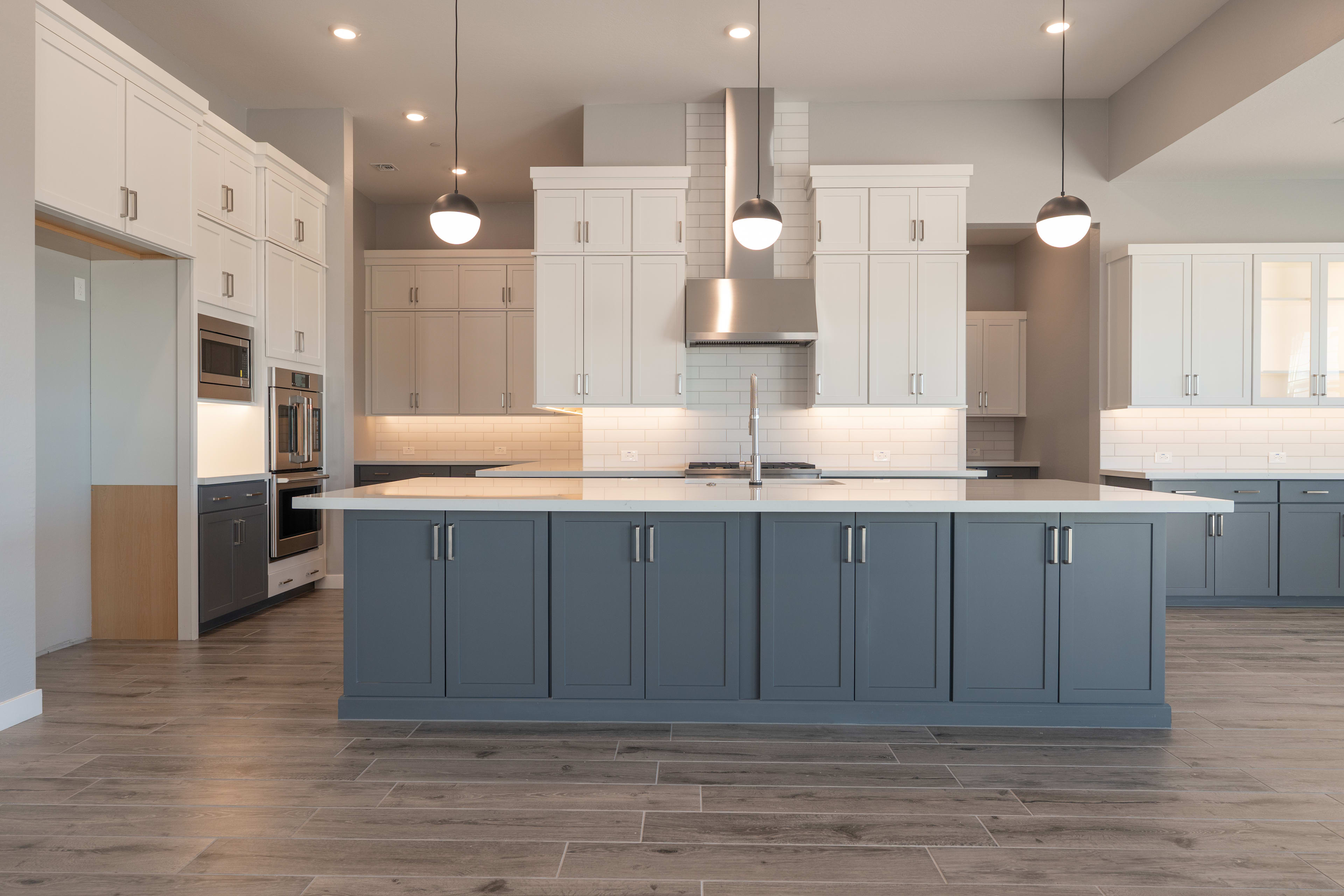 A modern and spacious kitchen with white cabinets, a large gray island, and pendant lighting fixtures, set against a tiled floor.