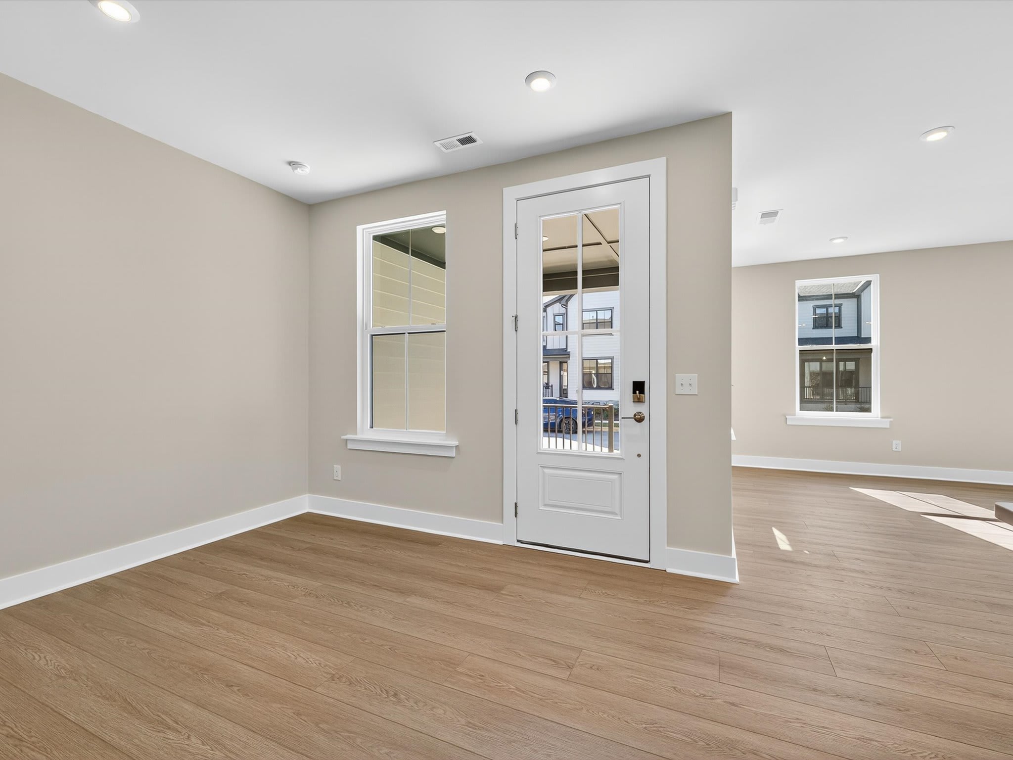 A bright and spacious room with a white door and windows, hardwood floors, and recessed lighting, creating a welcoming and modern atmosphere.