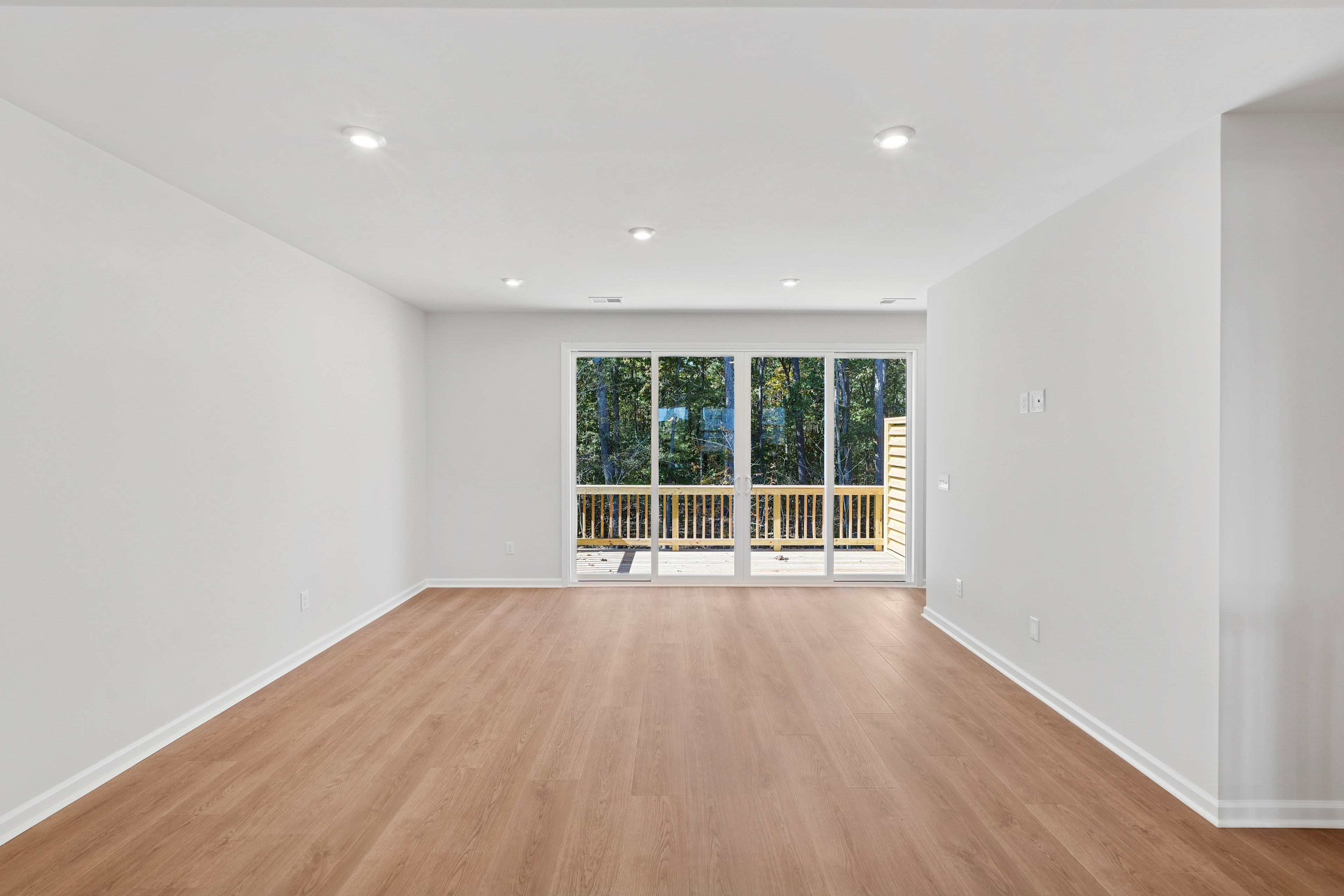 A spacious, well-lit room with a wooden floor and large windows overlooking a wooded area, creating a serene and inviting atmosphere.