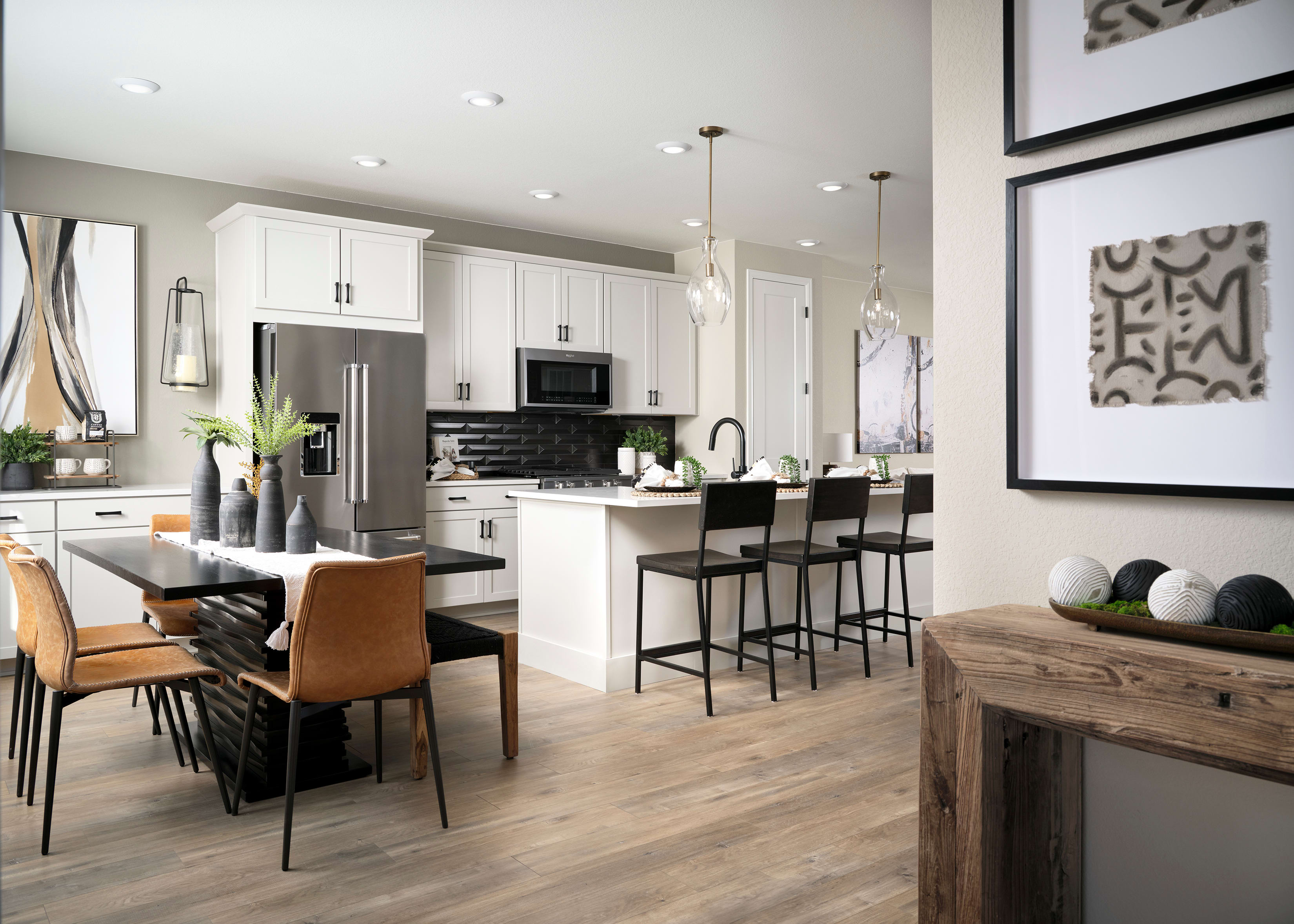 A modern, open-concept kitchen and dining area with white cabinets, stainless steel appliances, a wooden dining table, and pendant lighting.