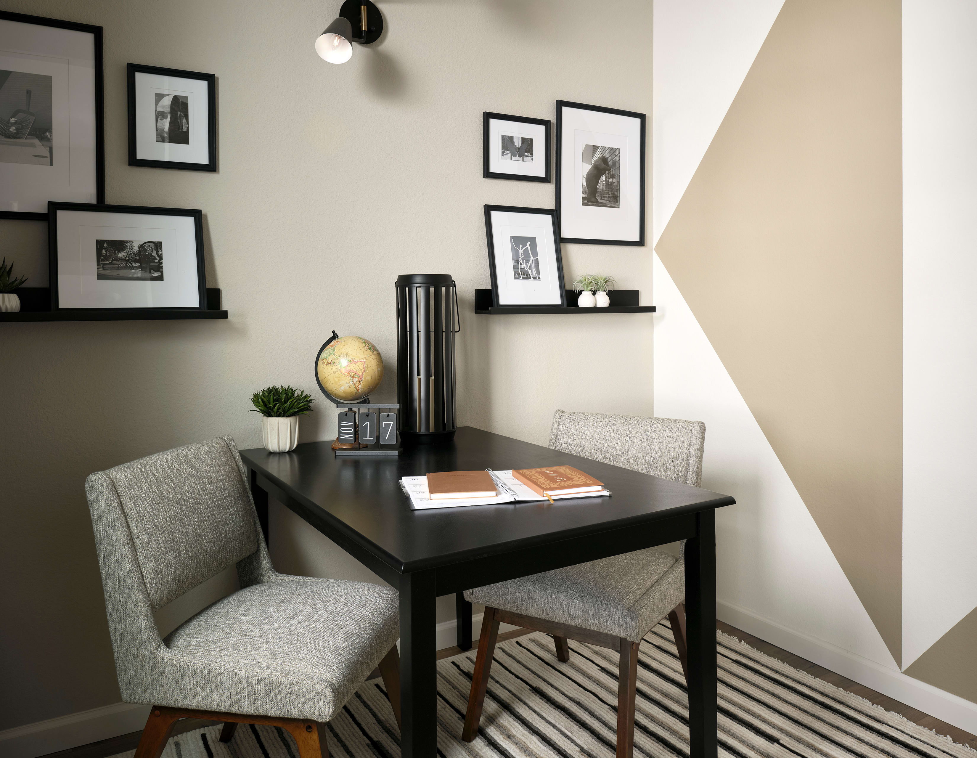 A modern and minimalist home office space with a dark wooden desk, gray upholstered chairs, and framed artwork displayed on the walls.