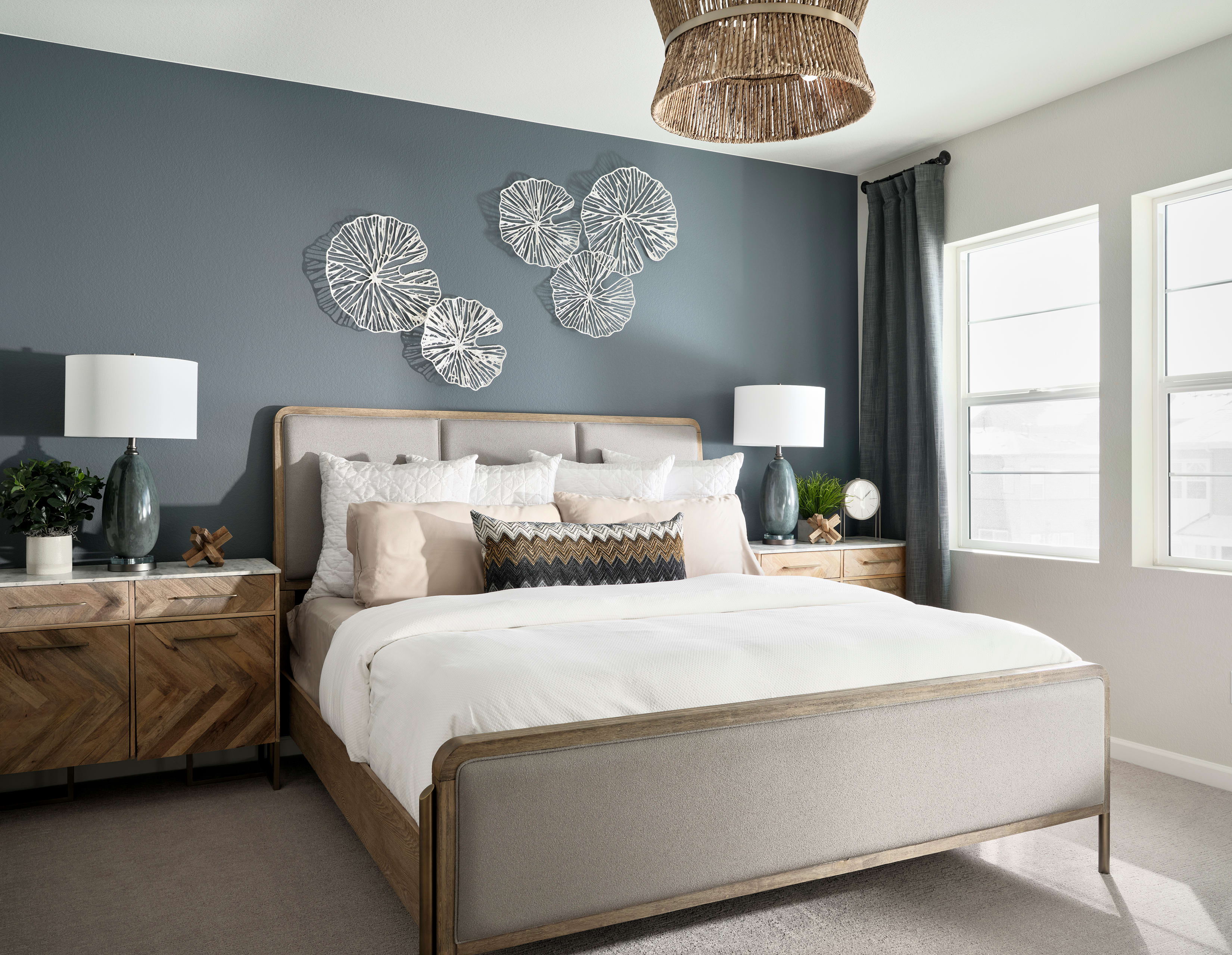 A cozy and stylish bedroom with a wooden bed frame, white bedding, and decorative wall art featuring abstract floral designs, complemented by a pendant light fixture and neutral-toned walls.