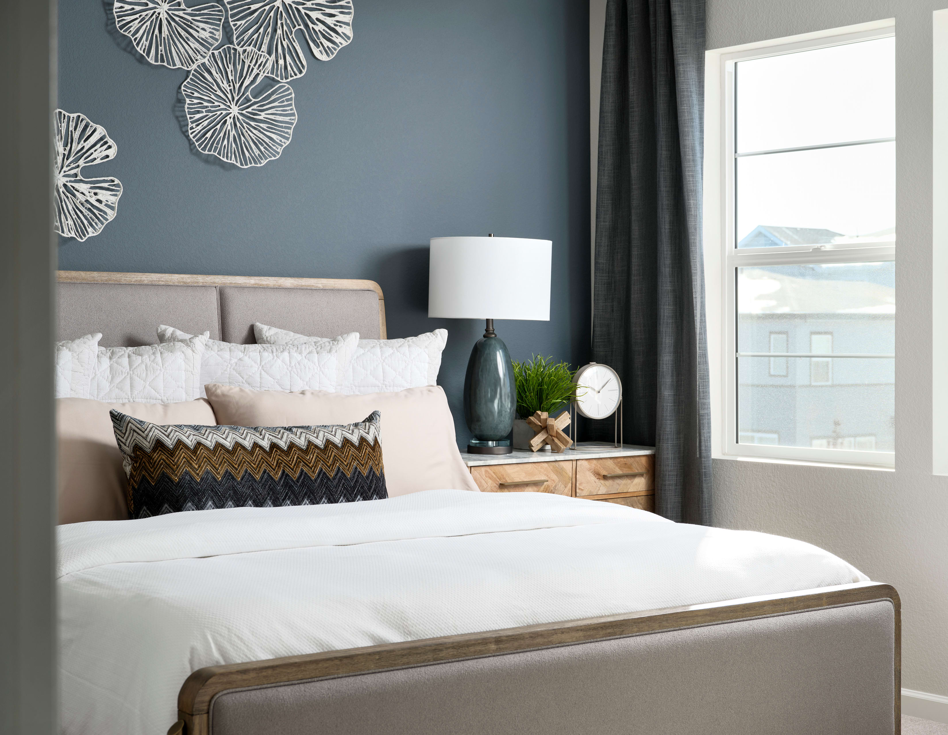 A cozy and modern bedroom with a large bed, a woven pendant light, and decorative wall art against a dark gray wall.