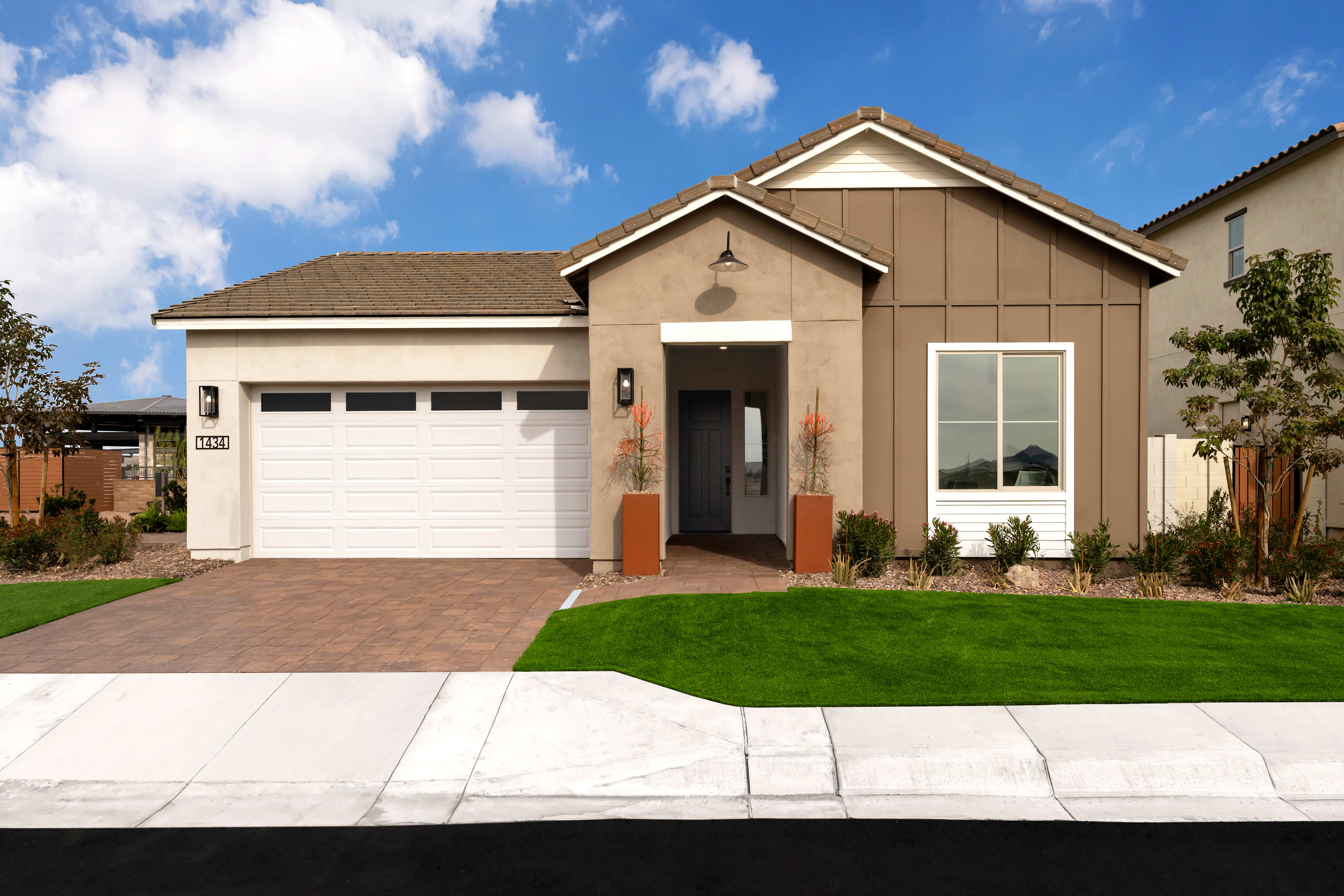 A single-story house with a garage, surrounded by a well-manicured lawn and a clear blue sky with fluffy white clouds.
