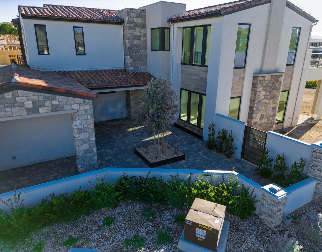 A modern, multi-story residential building with a landscaped yard, stone accents, and a garage in the foreground.