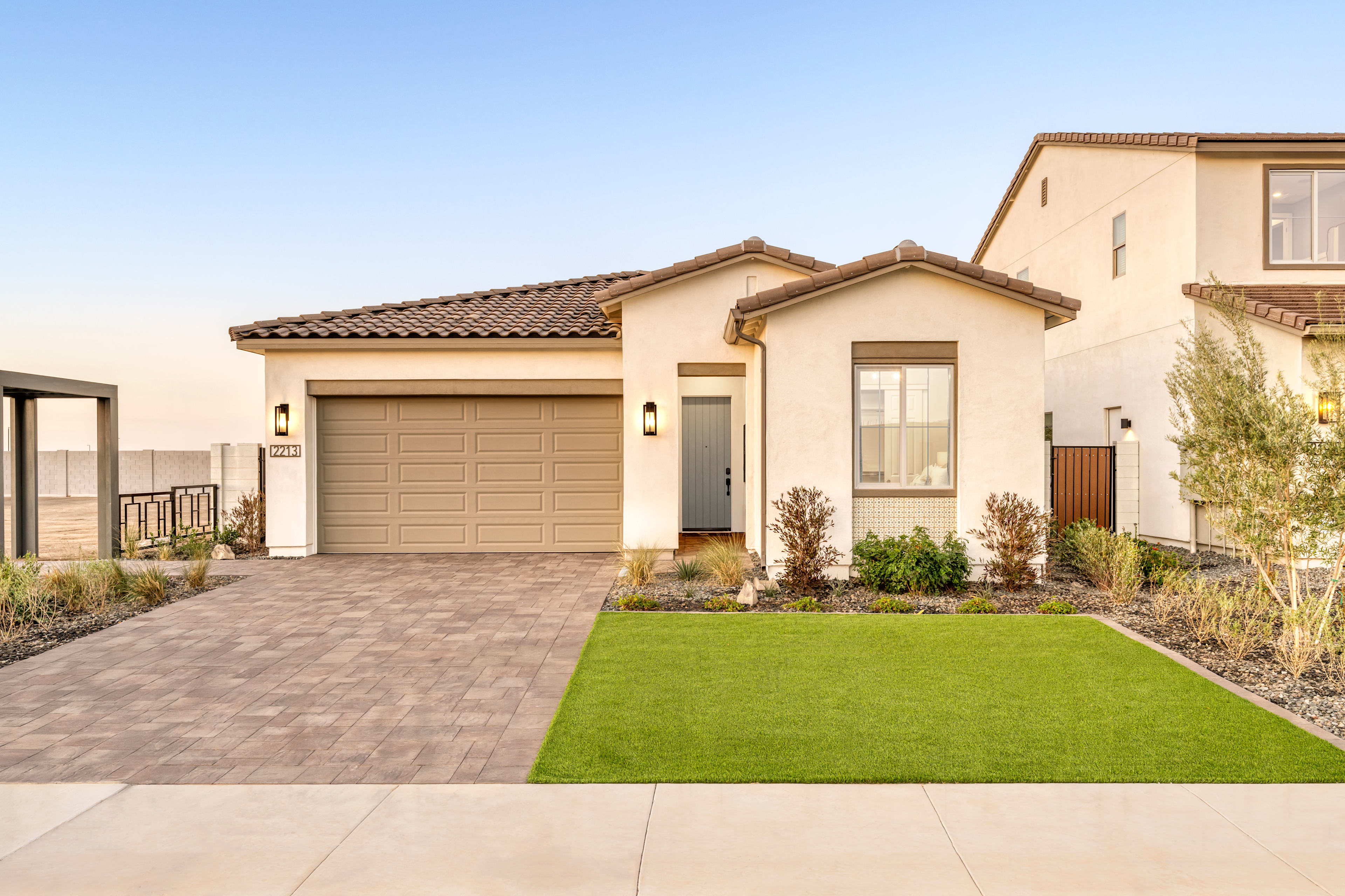 A single-story house with a tiled roof, a garage, and a well-manicured lawn in the foreground, set against a clear blue sky.