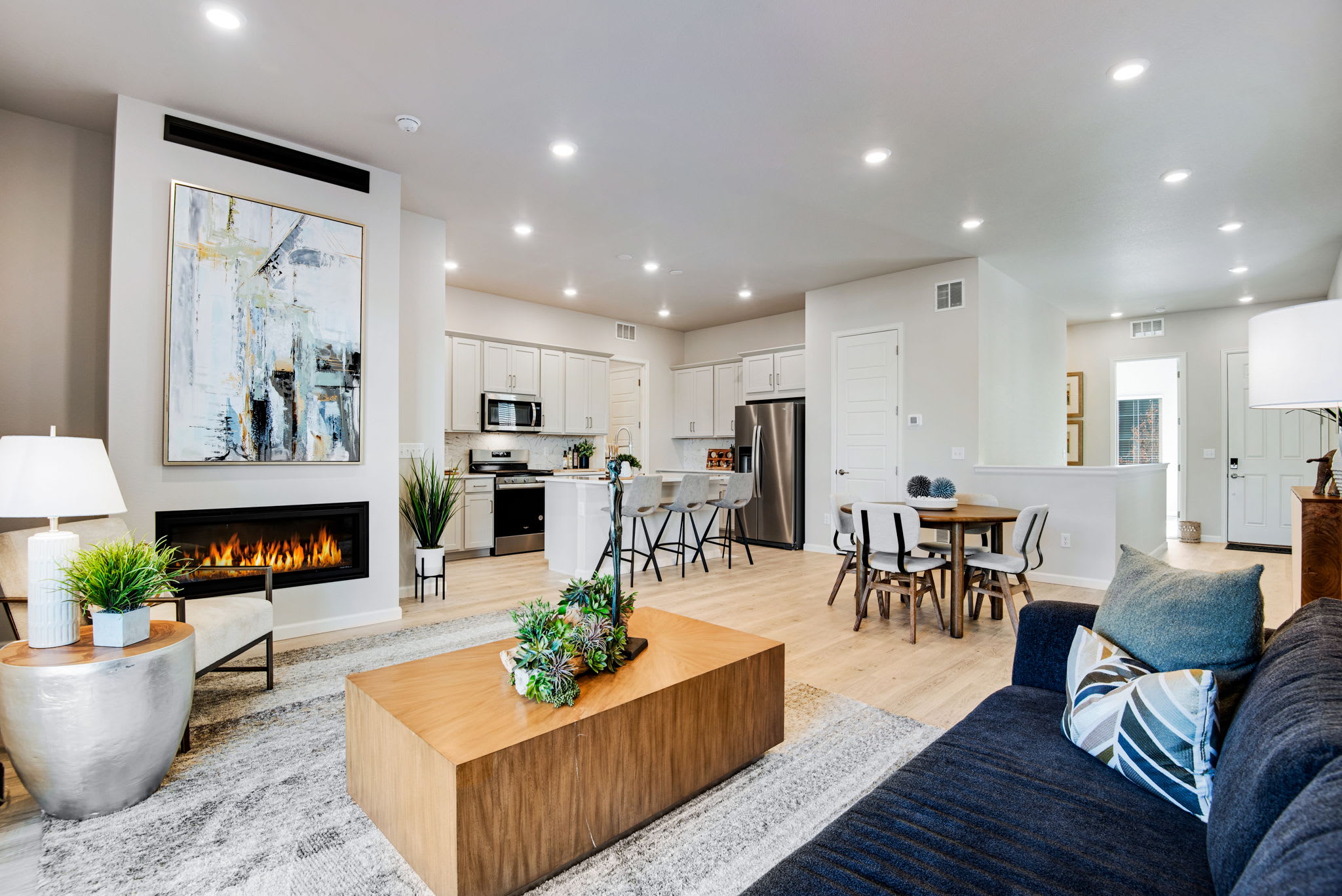 A modern and spacious open-concept living space with a fireplace, kitchen, dining area, and comfortable seating arrangements, all bathed in natural light.
