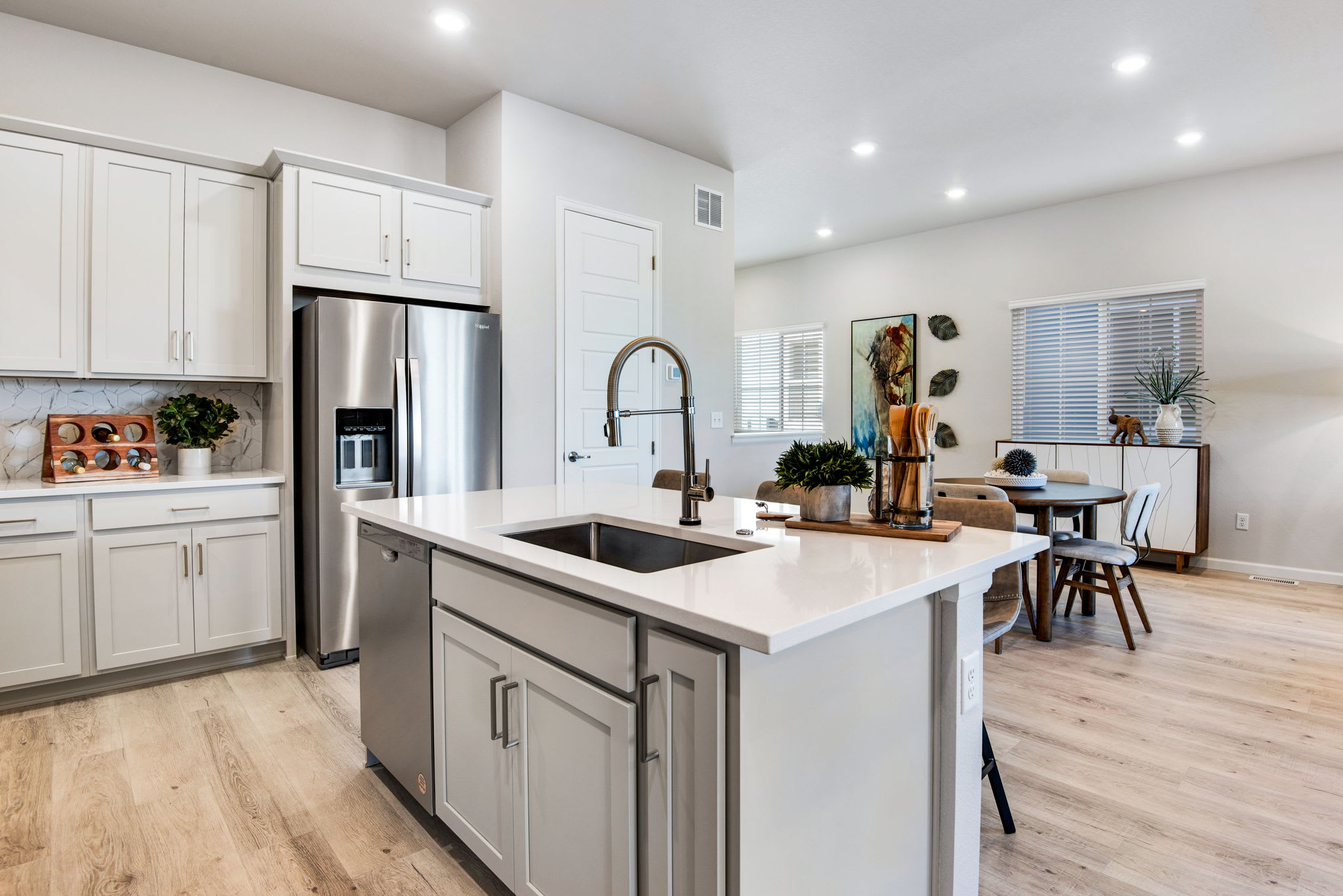 A modern, open-concept kitchen with white cabinets, a large island, and a dining area visible in the background.