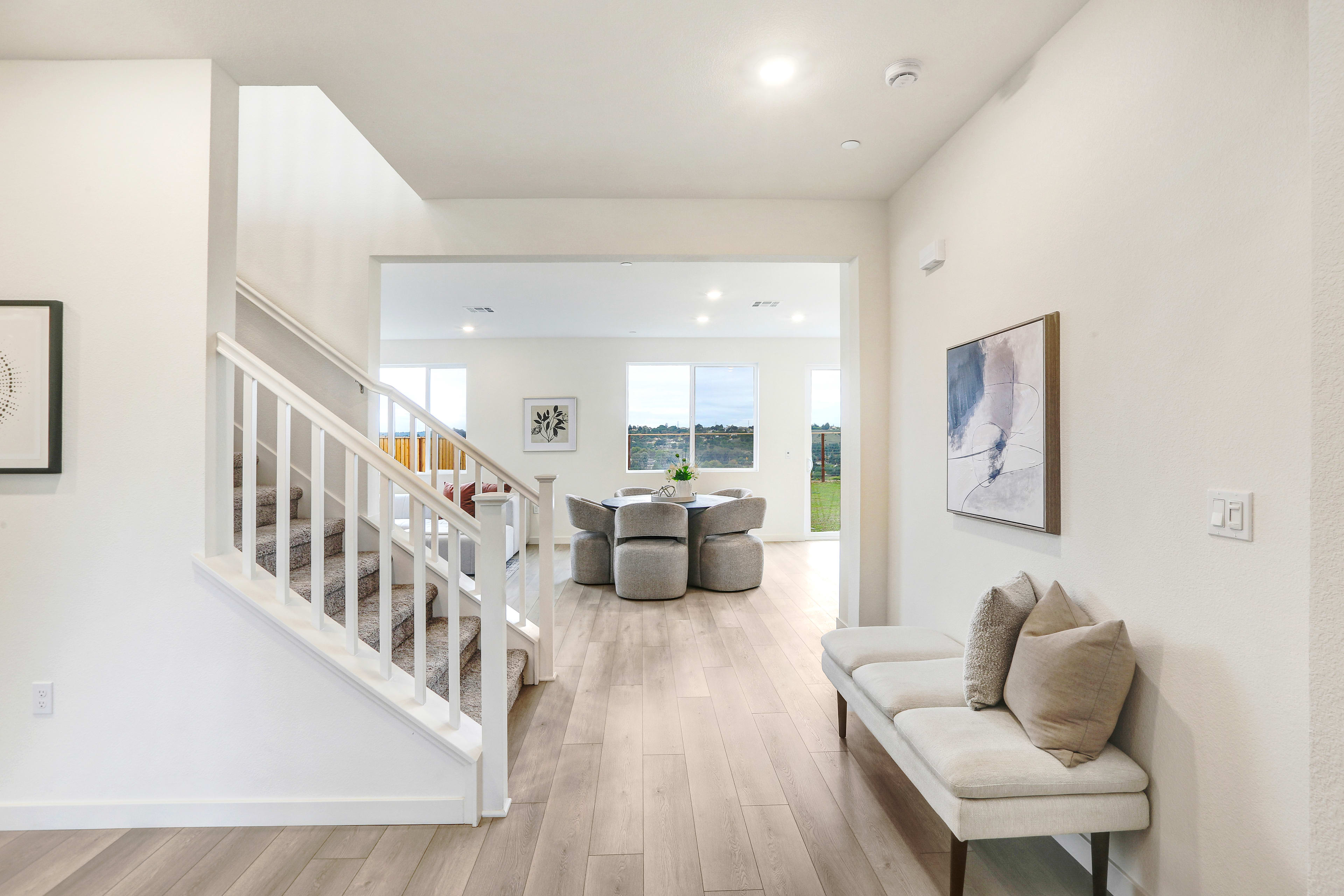 A bright and airy interior with a staircase leading to an open living area, featuring a couch and artwork on the walls.