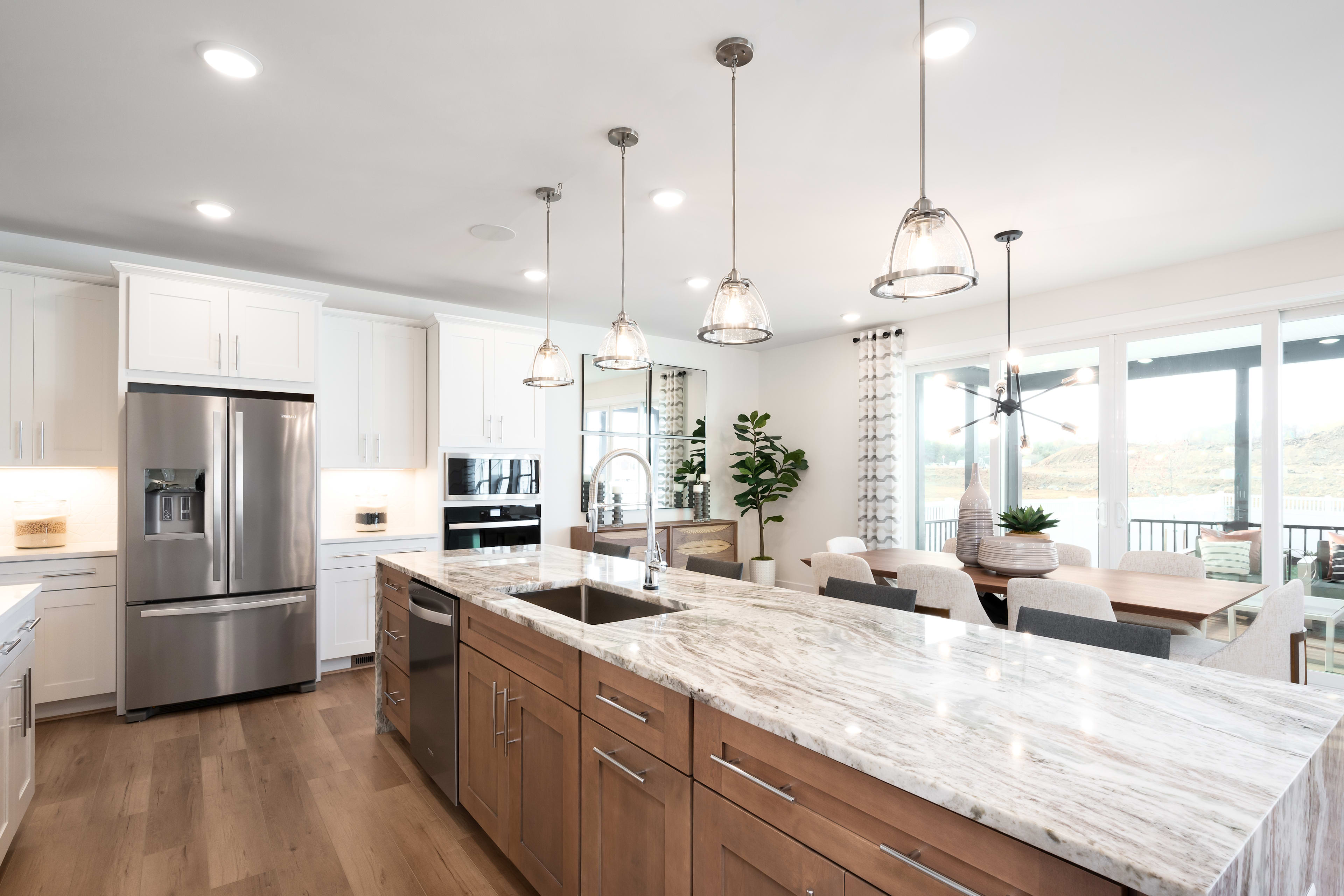 A modern, open-concept kitchen with white cabinets, wooden island countertop, and pendant lighting fixtures illuminating the space.