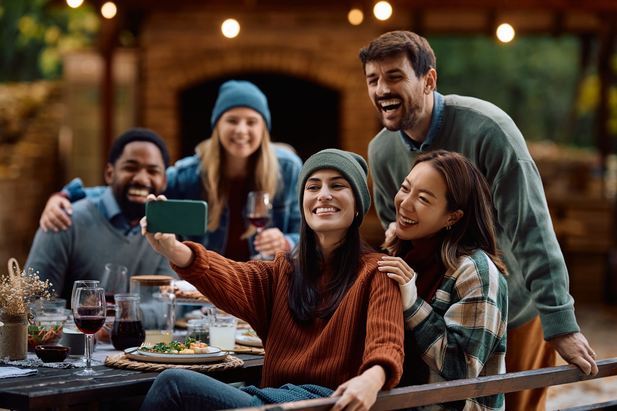 A group of friends enjoying a meal together outdoors, with string lights and a cozy atmosphere in the background.