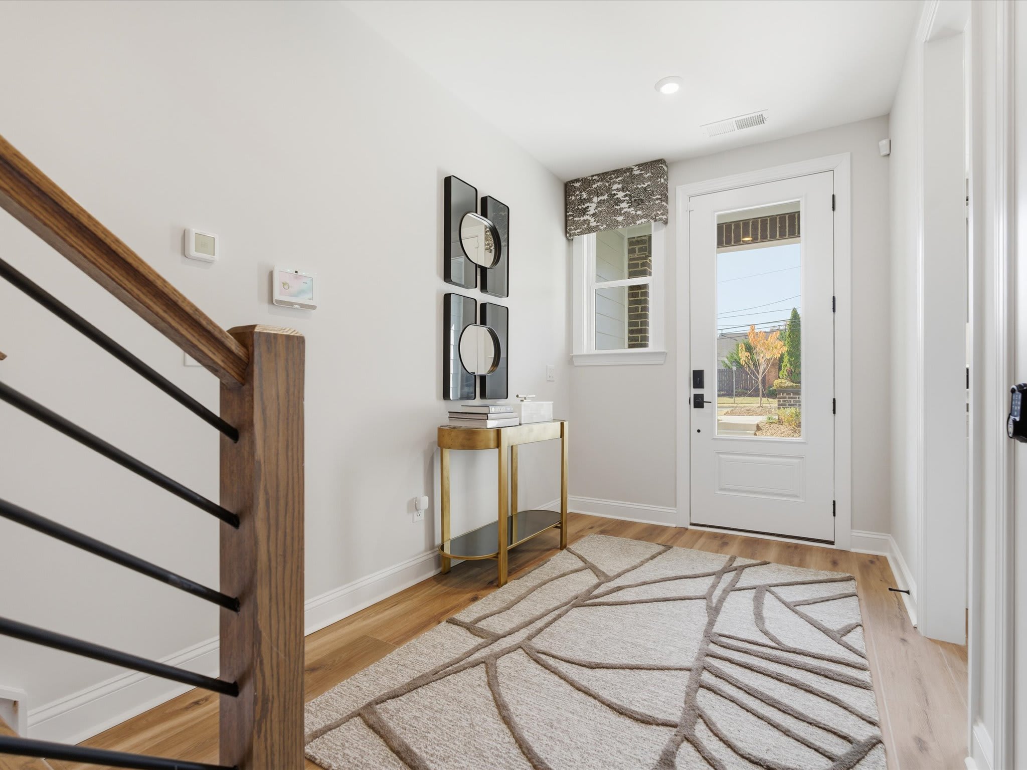 A modern and minimalist entryway with a wooden staircase, a patterned rug, and a decorative console table with a mirror display.