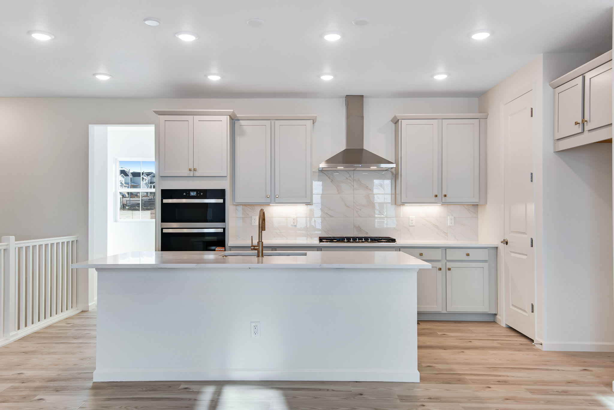 A modern, bright kitchen with white cabinets, a central island, and hardwood floors.