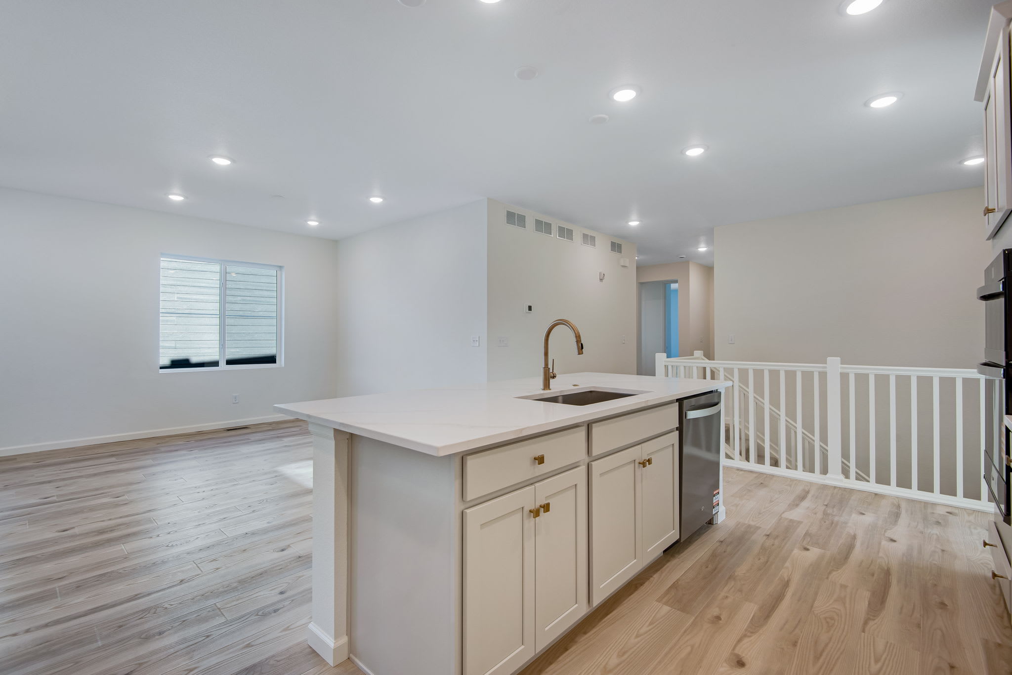 A modern, open-concept kitchen with white cabinets, a stainless steel appliance, and a wooden floor leading to a staircase with a railing.