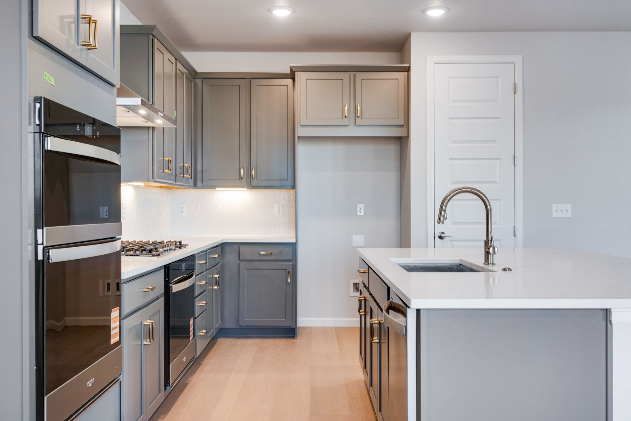 A modern, well-designed kitchen with gray cabinets, stainless steel appliances, and a white countertop island.