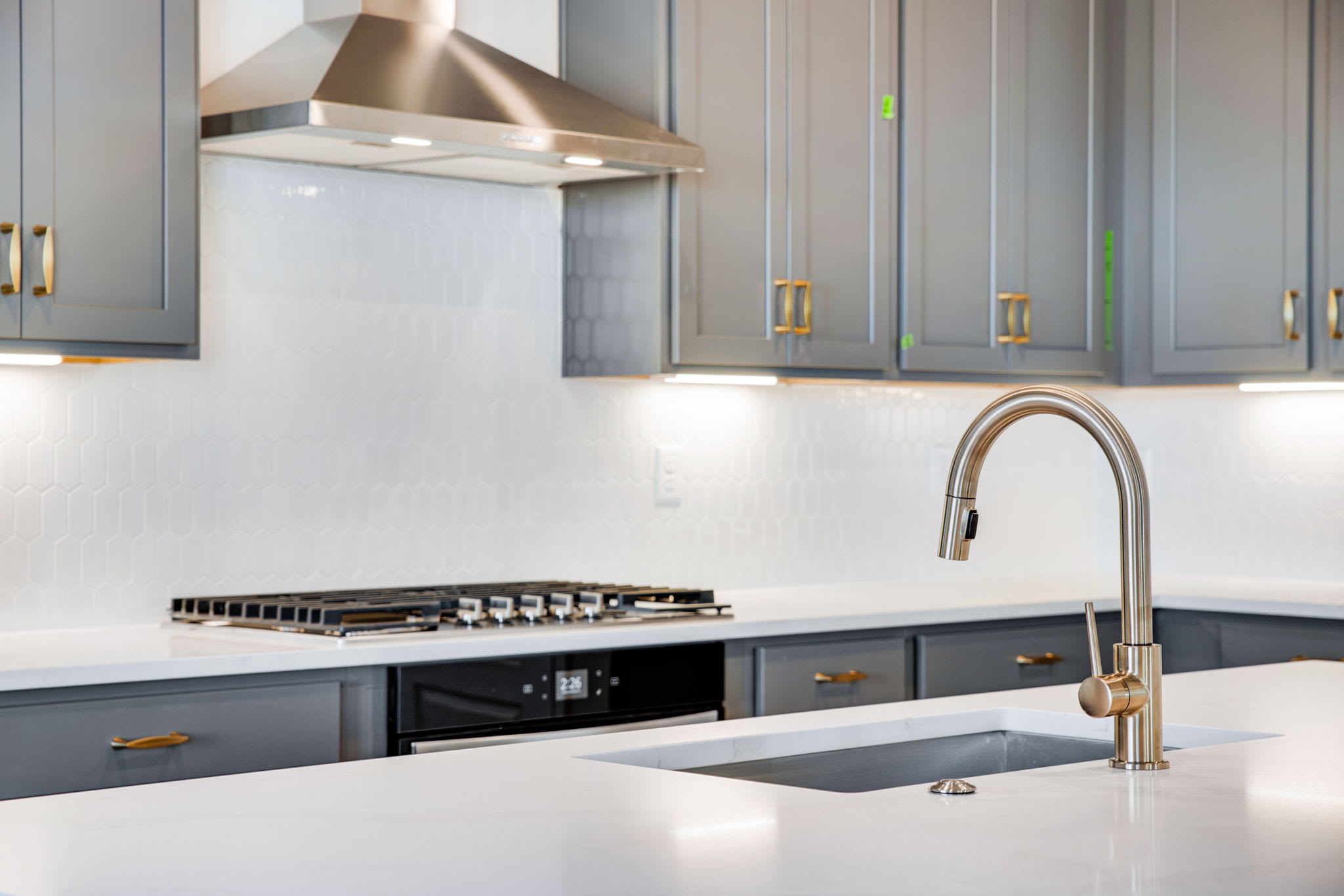 A modern kitchen with gray cabinets, a stainless steel range hood, and a sleek faucet over a white countertop.