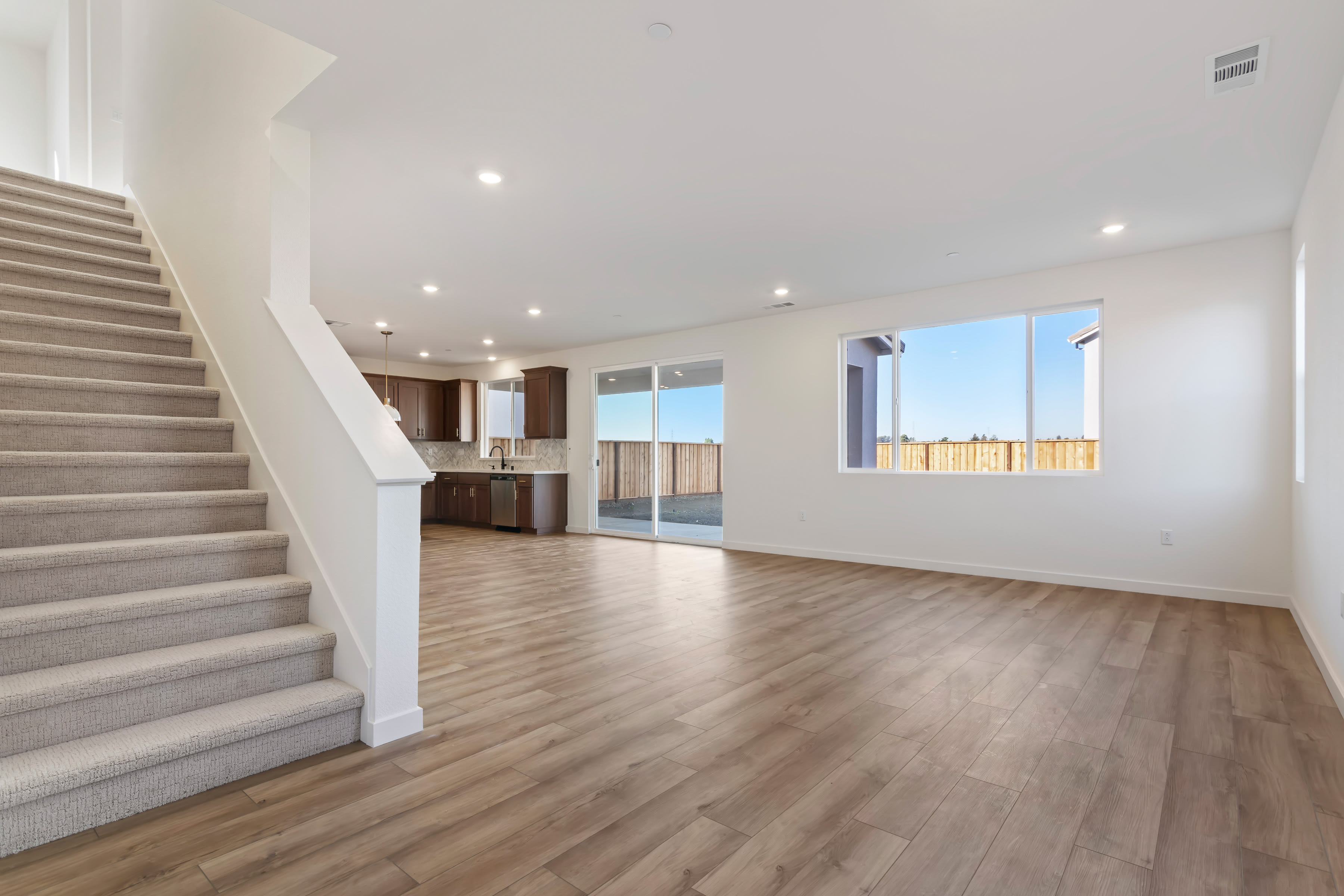 A spacious, open-concept living area with a staircase leading to an upper level, hardwood flooring, and large windows providing ample natural light.