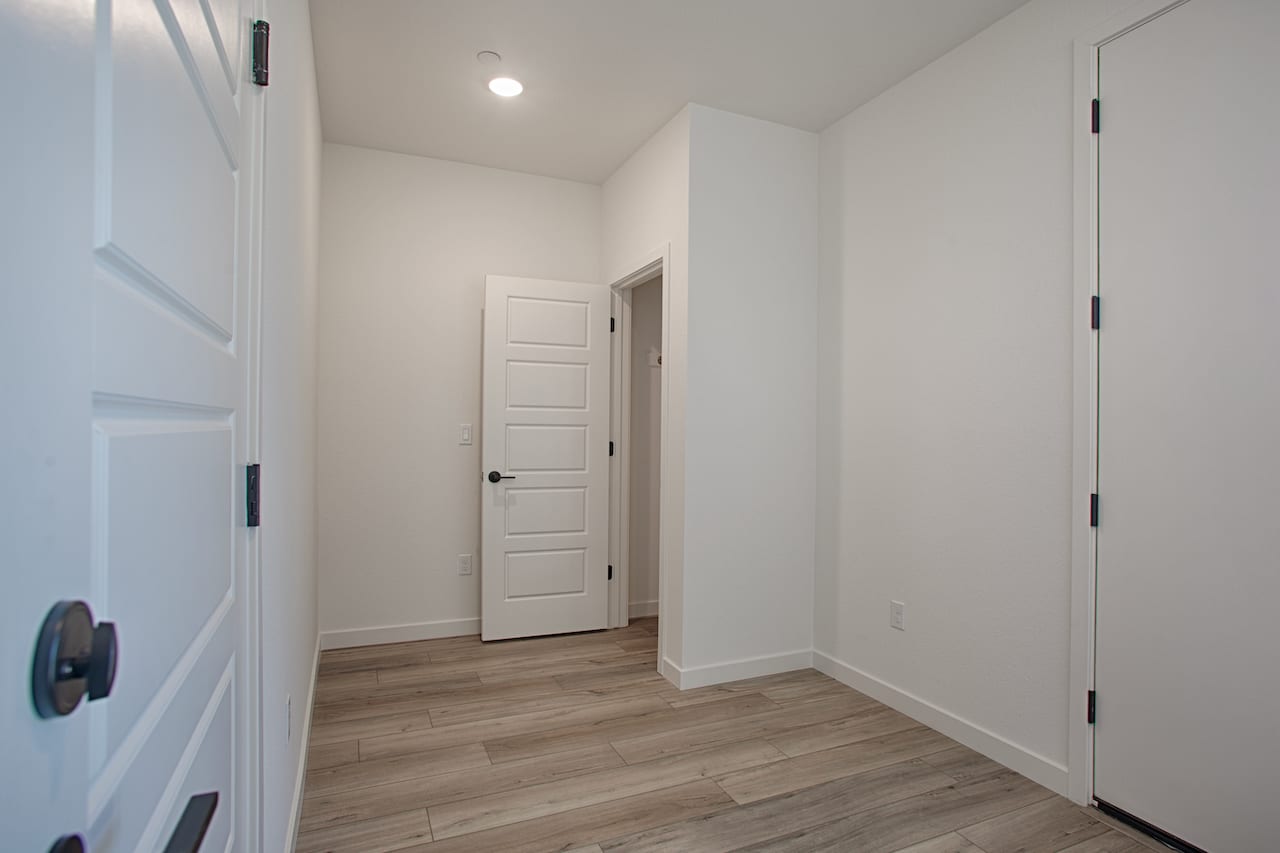 A bright, minimalist hallway with white walls, a wooden floor, and several closed doors leading to other rooms.