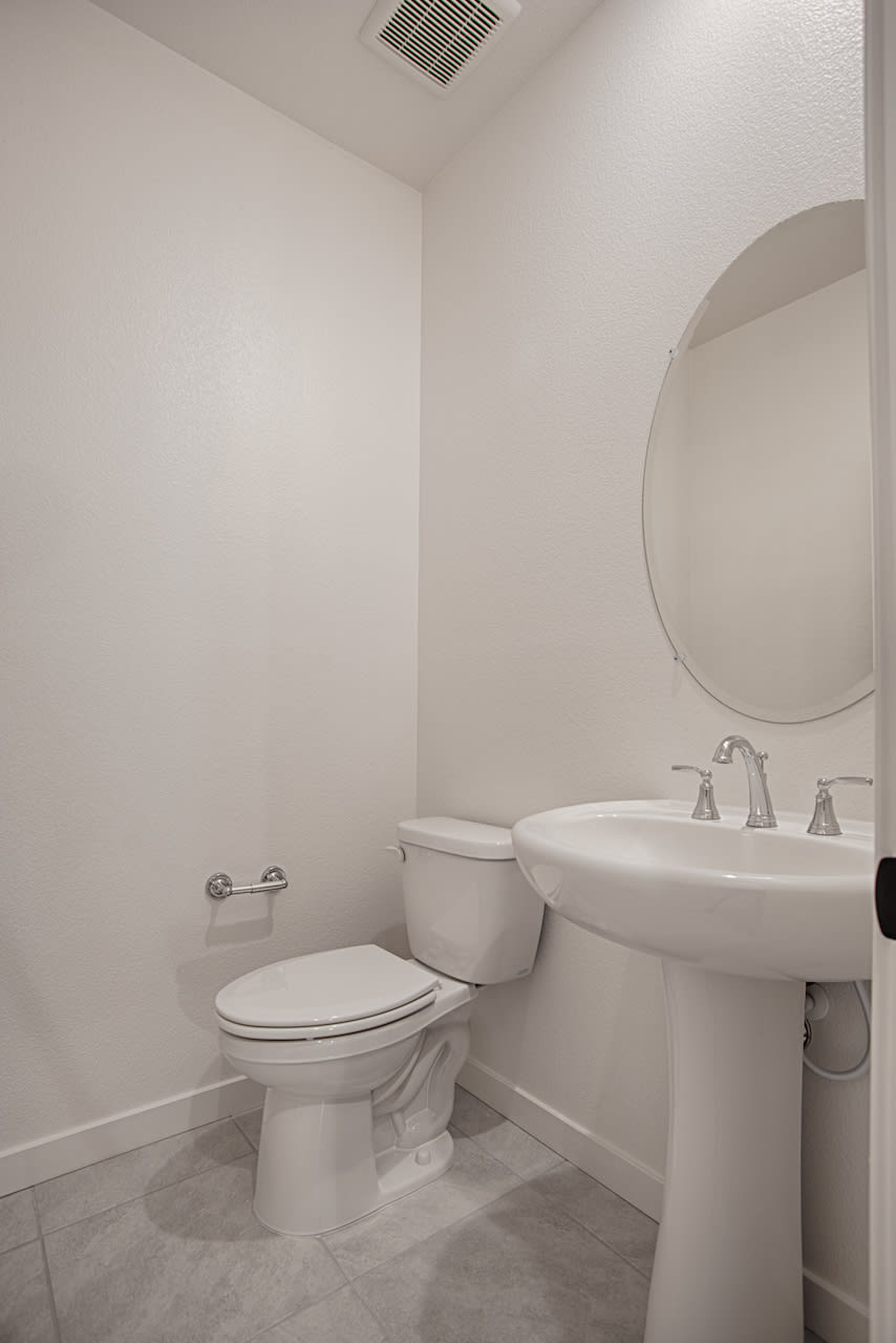 A clean, well-lit bathroom with a pedestal sink, toilet, and a round mirror on the wall.