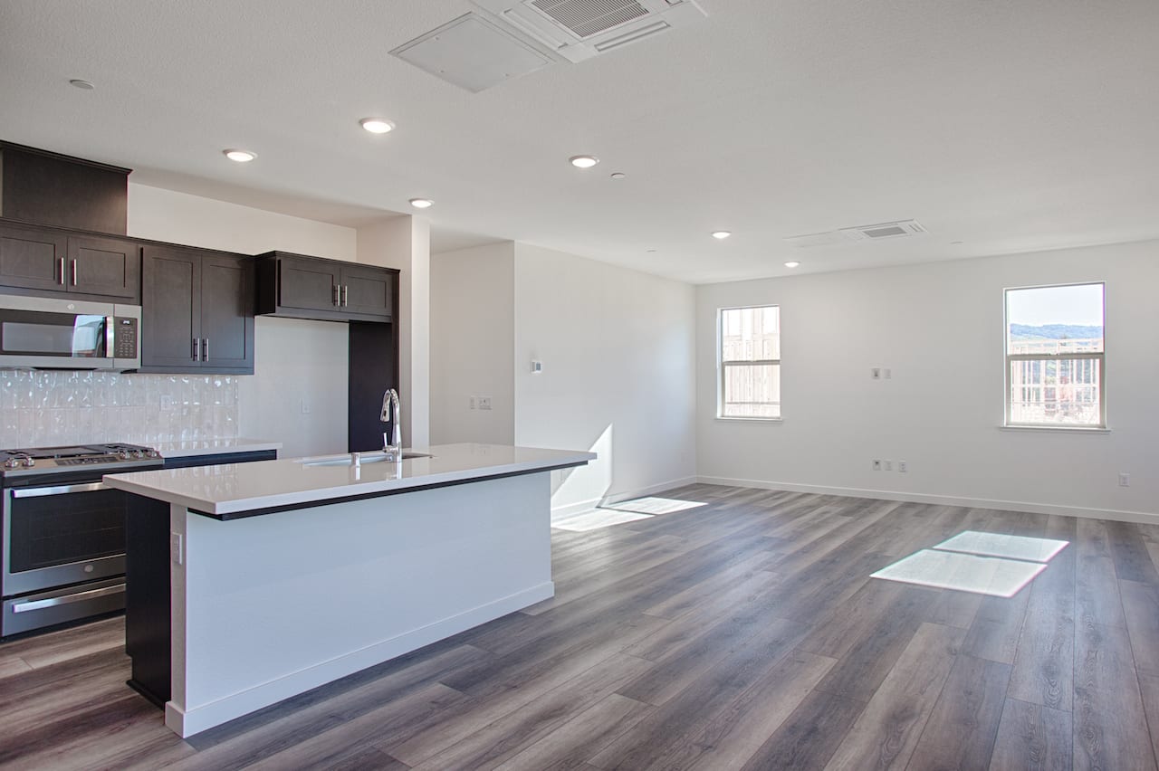 A modern, open-concept kitchen and living room with dark wood cabinets, a white island, and hardwood floors.