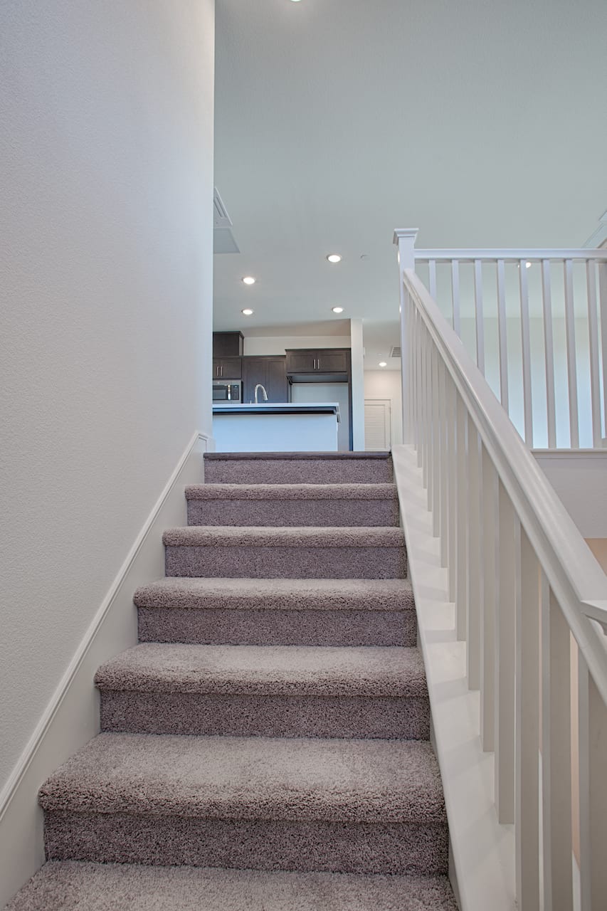The image shows a staircase with white railings leading up to a kitchen area in the background.