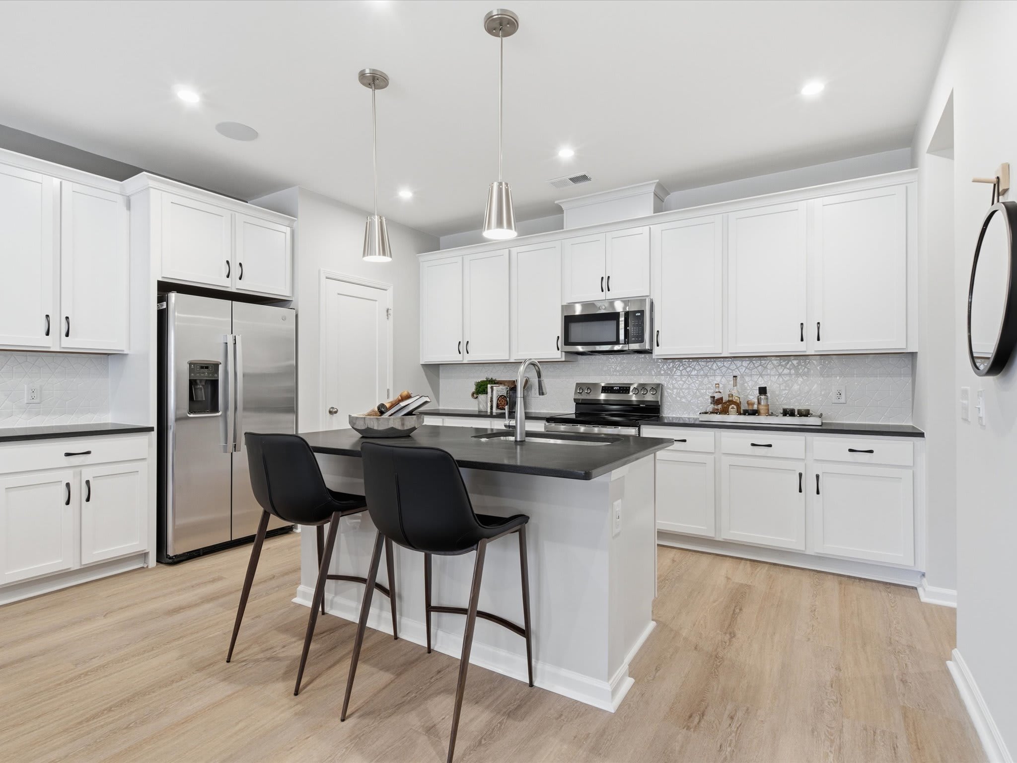 A modern, well-lit kitchen with white cabinets, stainless steel appliances, and a central island with bar stools, set against a hardwood floor.
