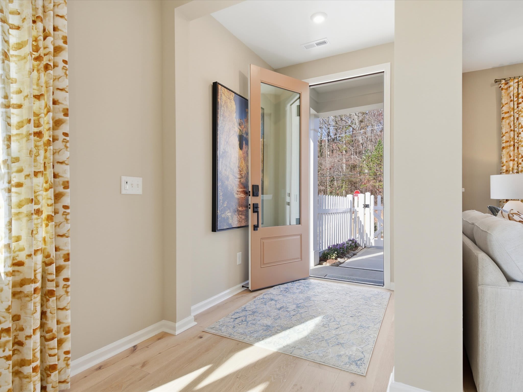 A bright and airy hallway with a wooden door leading to the outdoors, adorned with patterned curtains and a decorative rug on the floor.