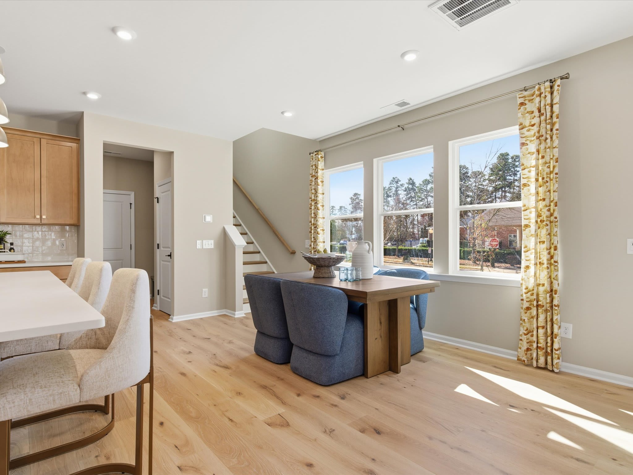 A cozy and bright living room with hardwood floors, a dining table, and large windows overlooking a scenic outdoor view.